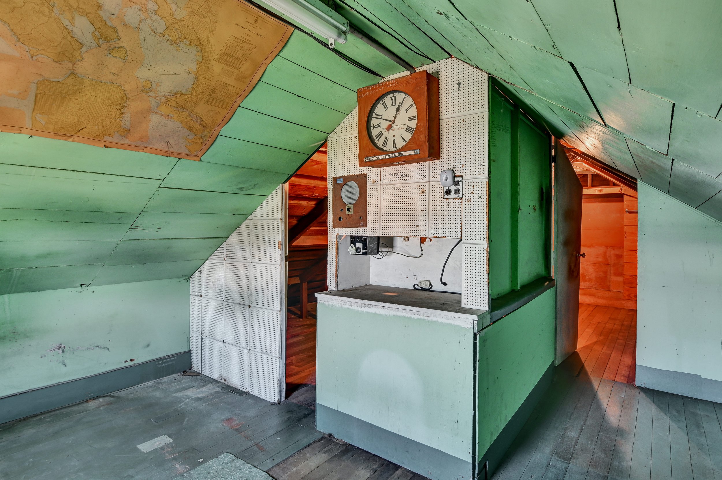 An attic space with green painted walls and slanted ceiling, featuring an old circular wall clock, a map on the ceiling, and a small indoor water fountain or sink area.