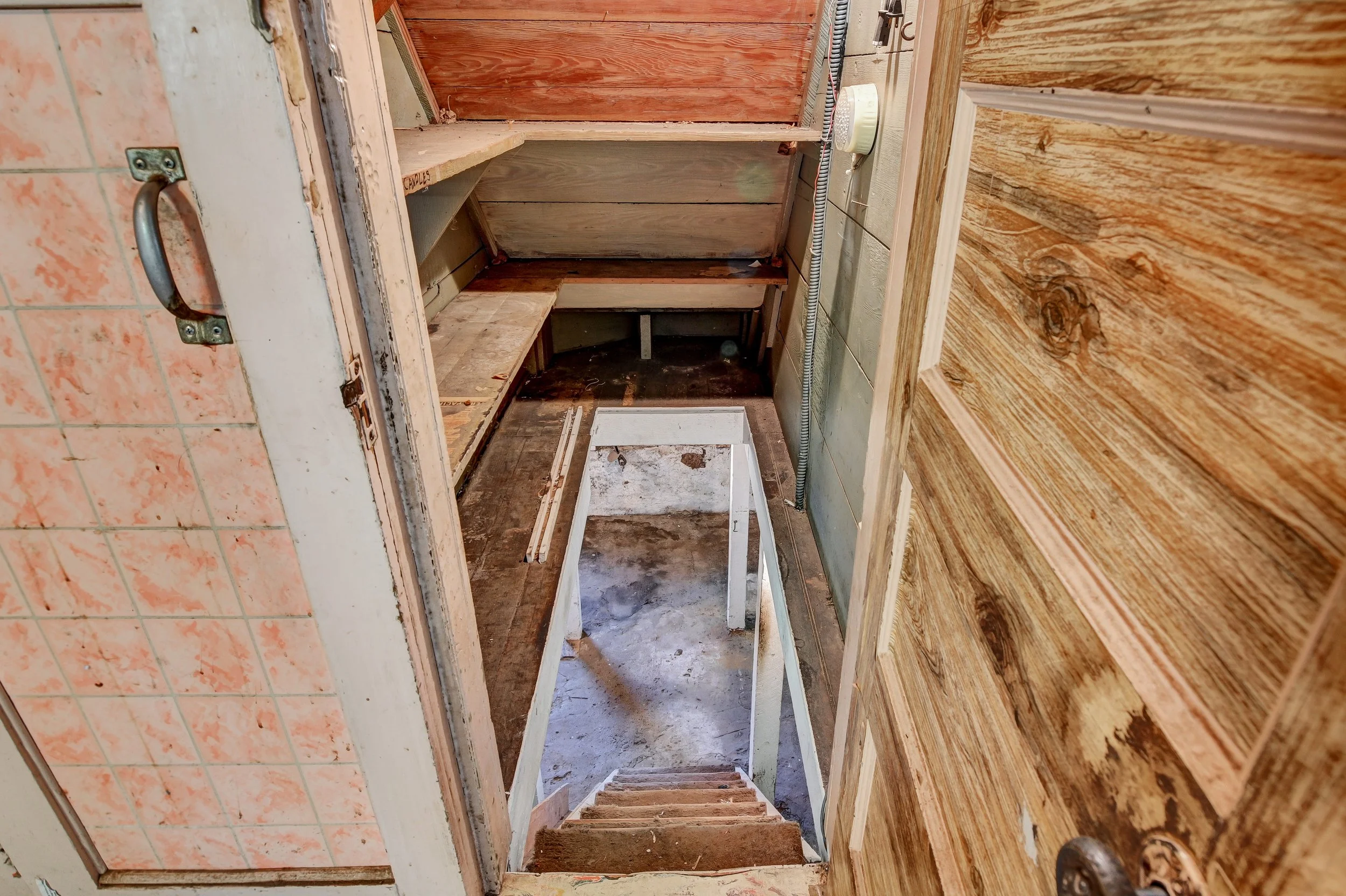 Empty small storage or closet space with wooden shelves on the left and right sides, a staircase leading down, and various construction materials inside.