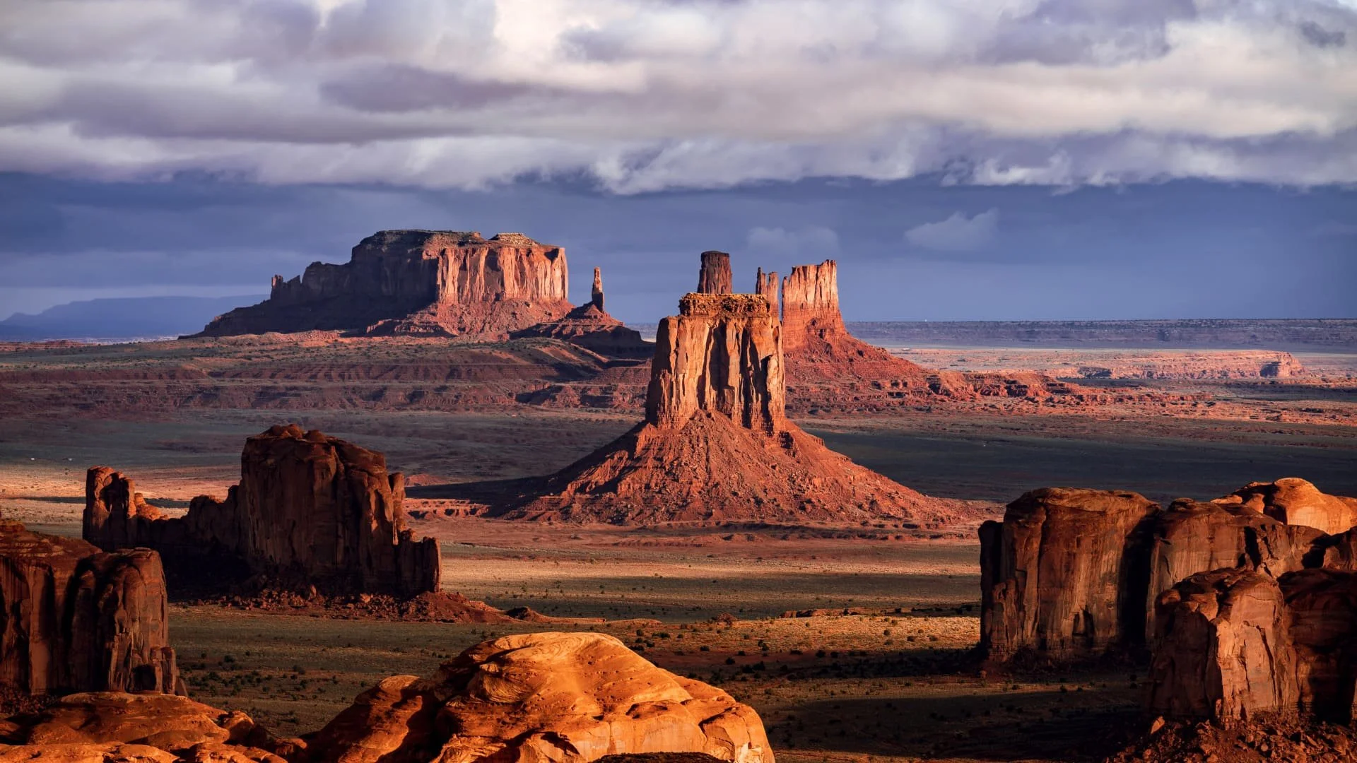 Desert landscape with rock formations and mesas under a cloudy sky.
