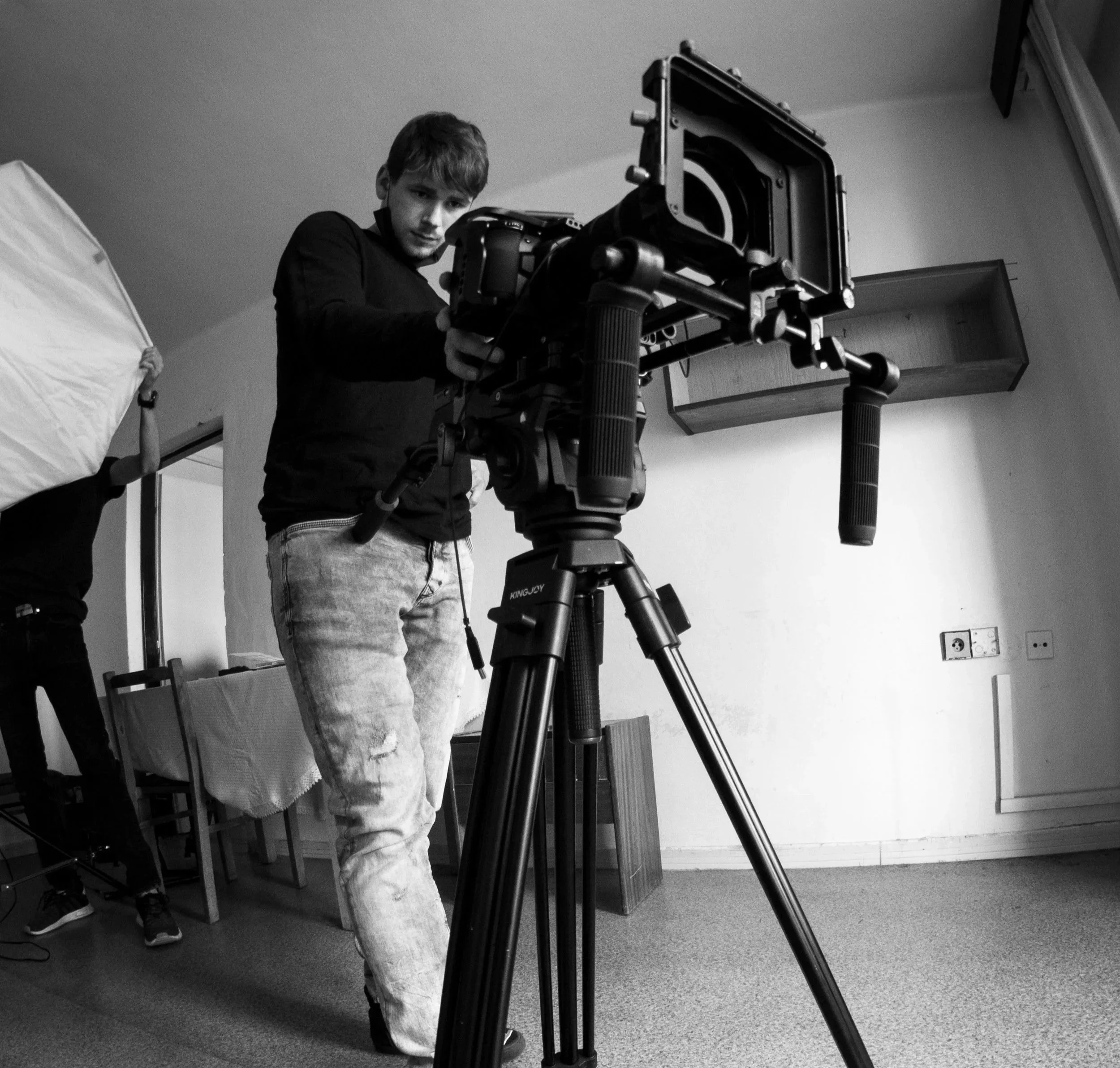 A person setting up a professional video camera on a tripod in an indoor studio or room.