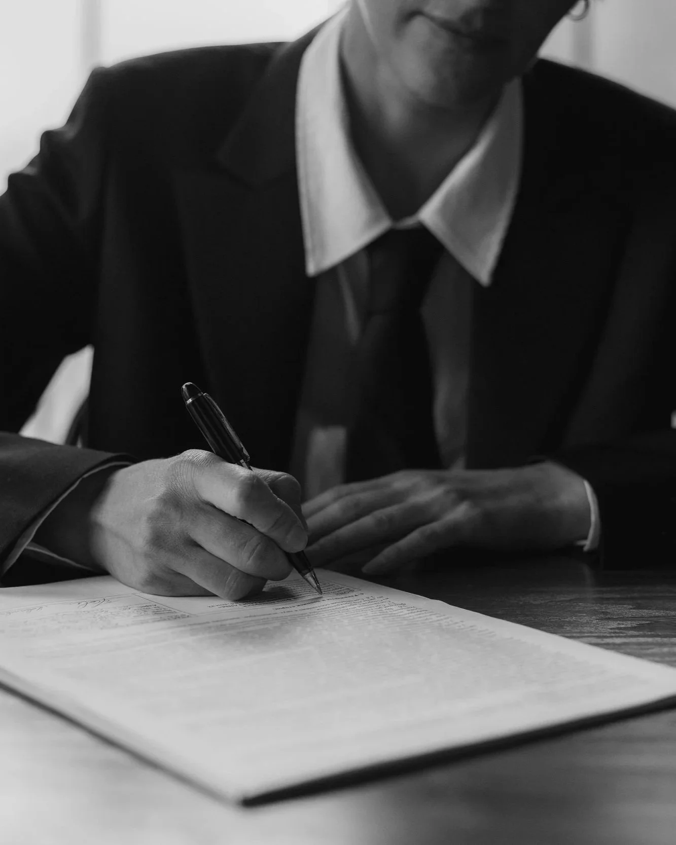 A person in a suit signing a document with a pen, black and white photo.