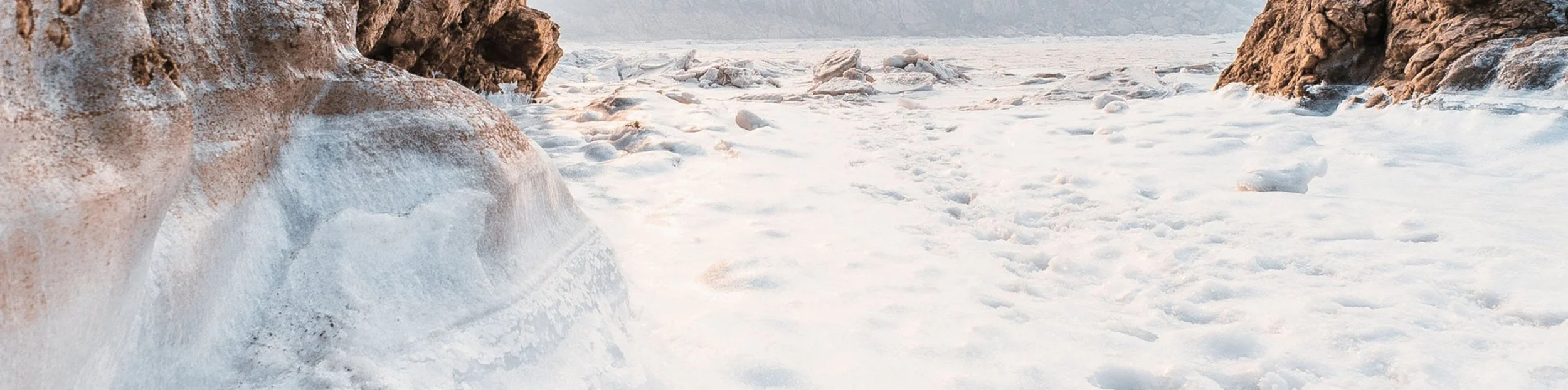 Ice and snow covering the ground between rocky cliffs, with snow and ice formations visible on the rocks.