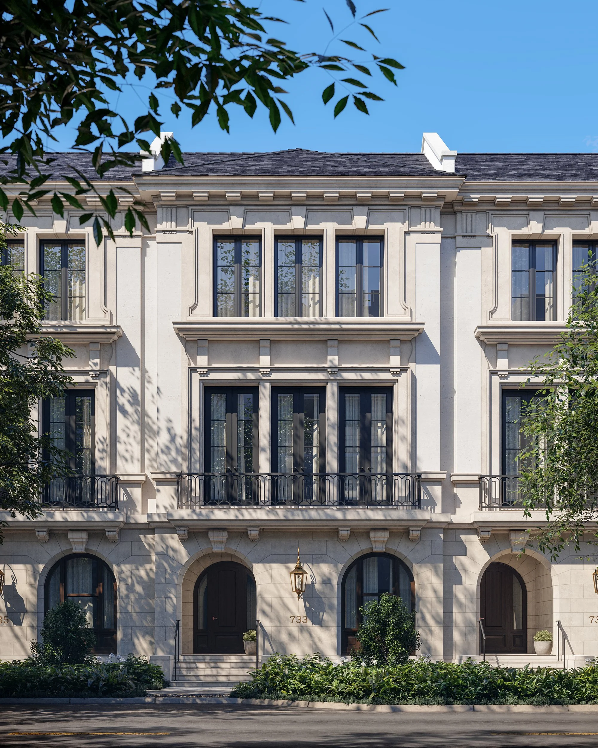 A white multi-story building with arched windows, decorative molding, and a balcony with a black wrought-iron railing. The entrance has dark double doors numbered 733, and there is a street lamp hanging above the stairway. Green plants and trees part