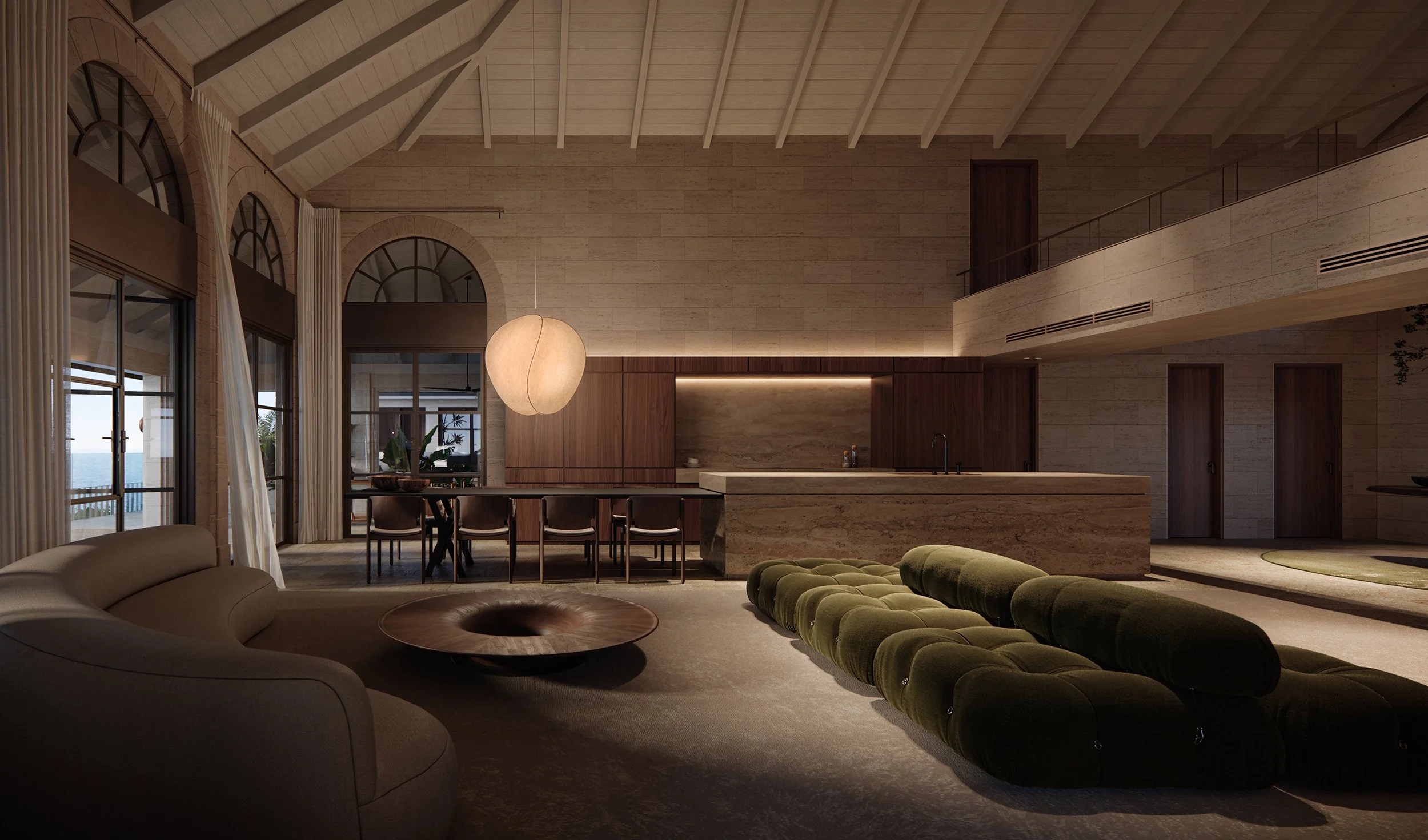 A spacious, modern living room with high vaulted ceiling, large arched windows with white curtains, and a view of the ocean outside. The room features a curved beige sofa, a large green tufted ottoman, a round wooden coffee table, and a dining area w