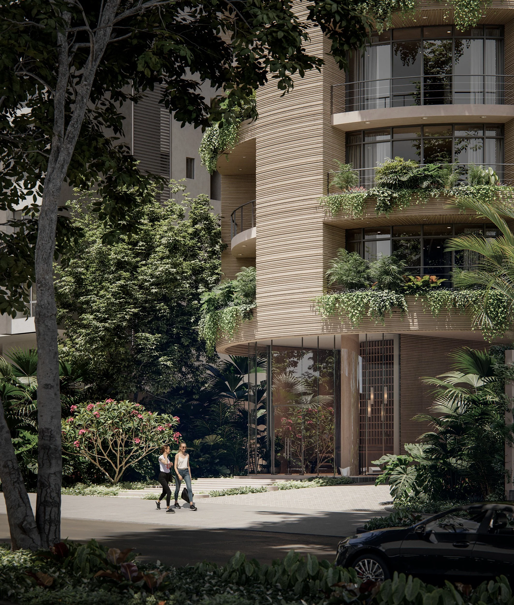 Two women walking and talking on a sidewalk outside a modern building with large glass windows, surrounded by lush greenery and trees.