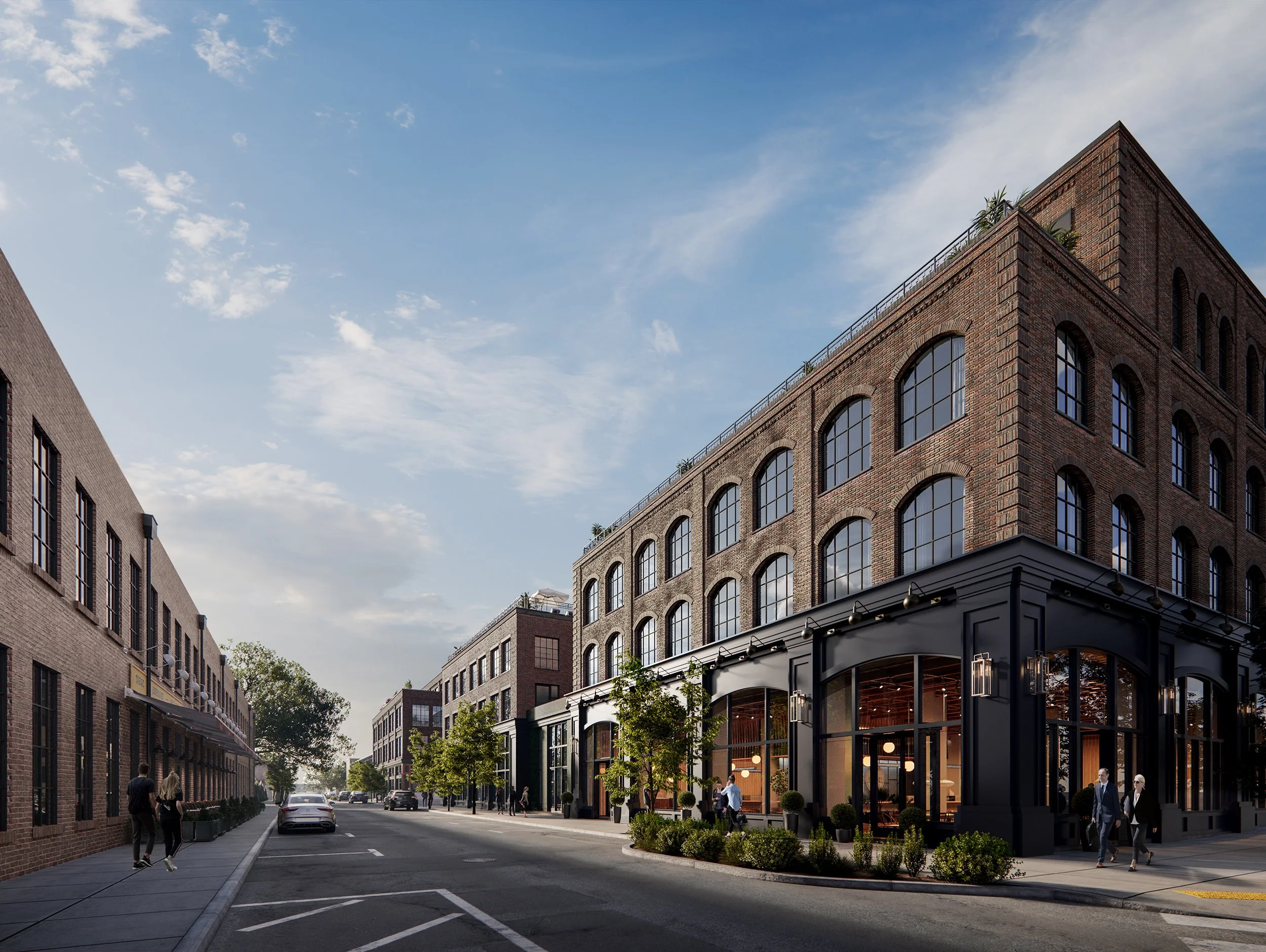 City street with modern brick buildings, small trees, parked cars, and pedestrians, under a partly cloudy sky.