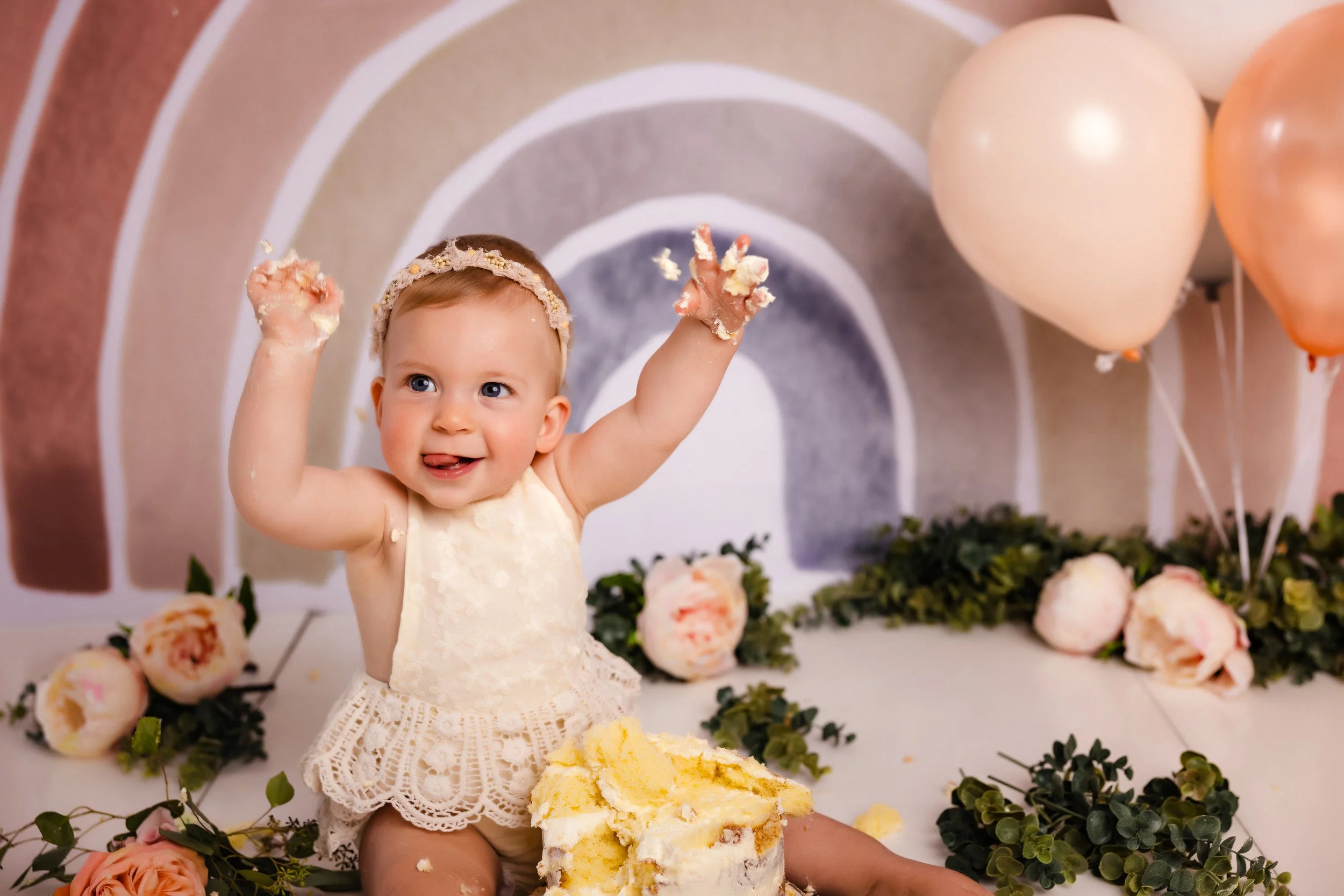 A young girl celebrating her birthday with a cake, surrounded by flowers and balloons, with cake on her hands and face.