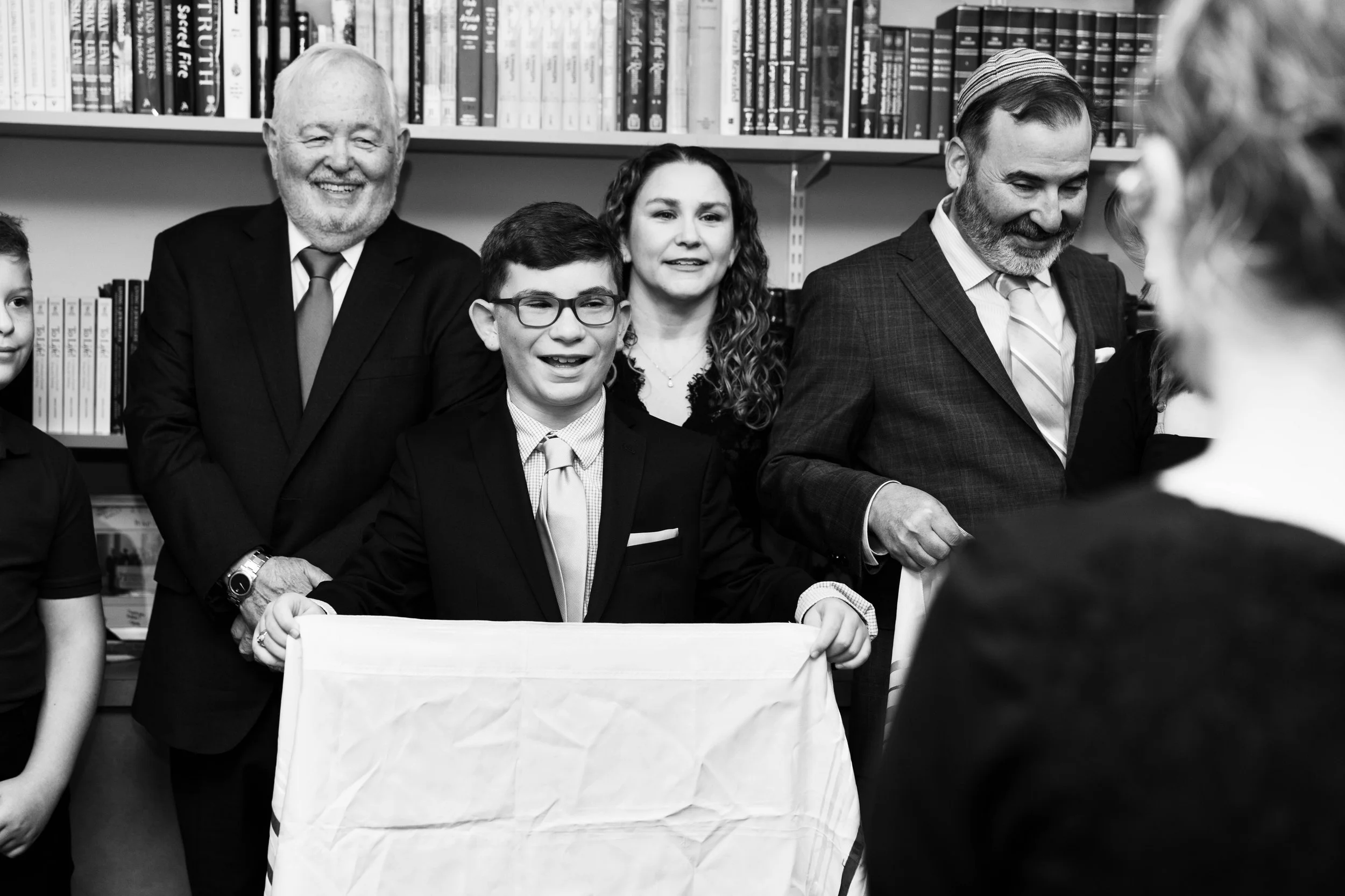 A group of people gathered, including a young man holding a cloth, and others smiling, in front of a bookshelf filled with books.