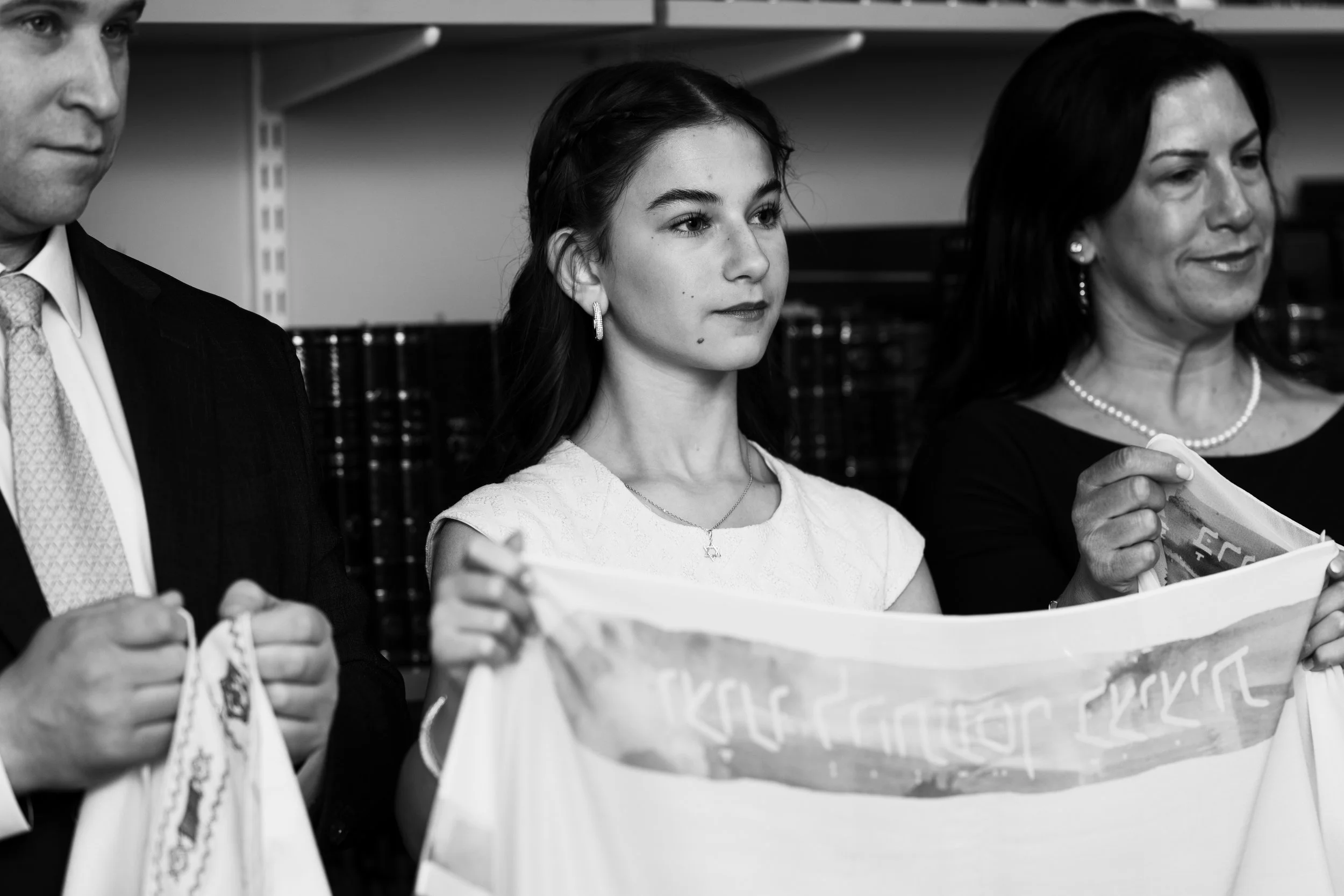 Three individuals, a man and two women, standing in a row holding a banner or flag in an indoor setting. The image is in black and white.