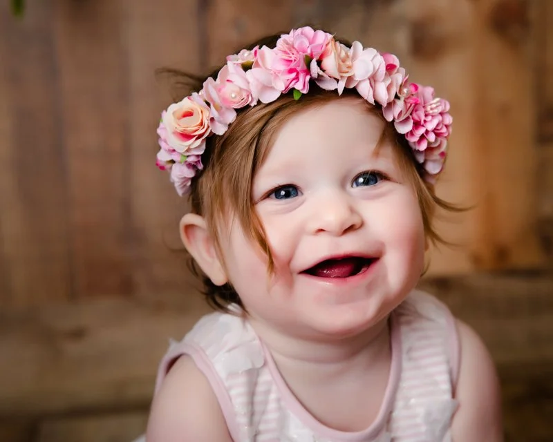 A smiling young girl with red hair wearing a flower crown made of pink and peach flowers.