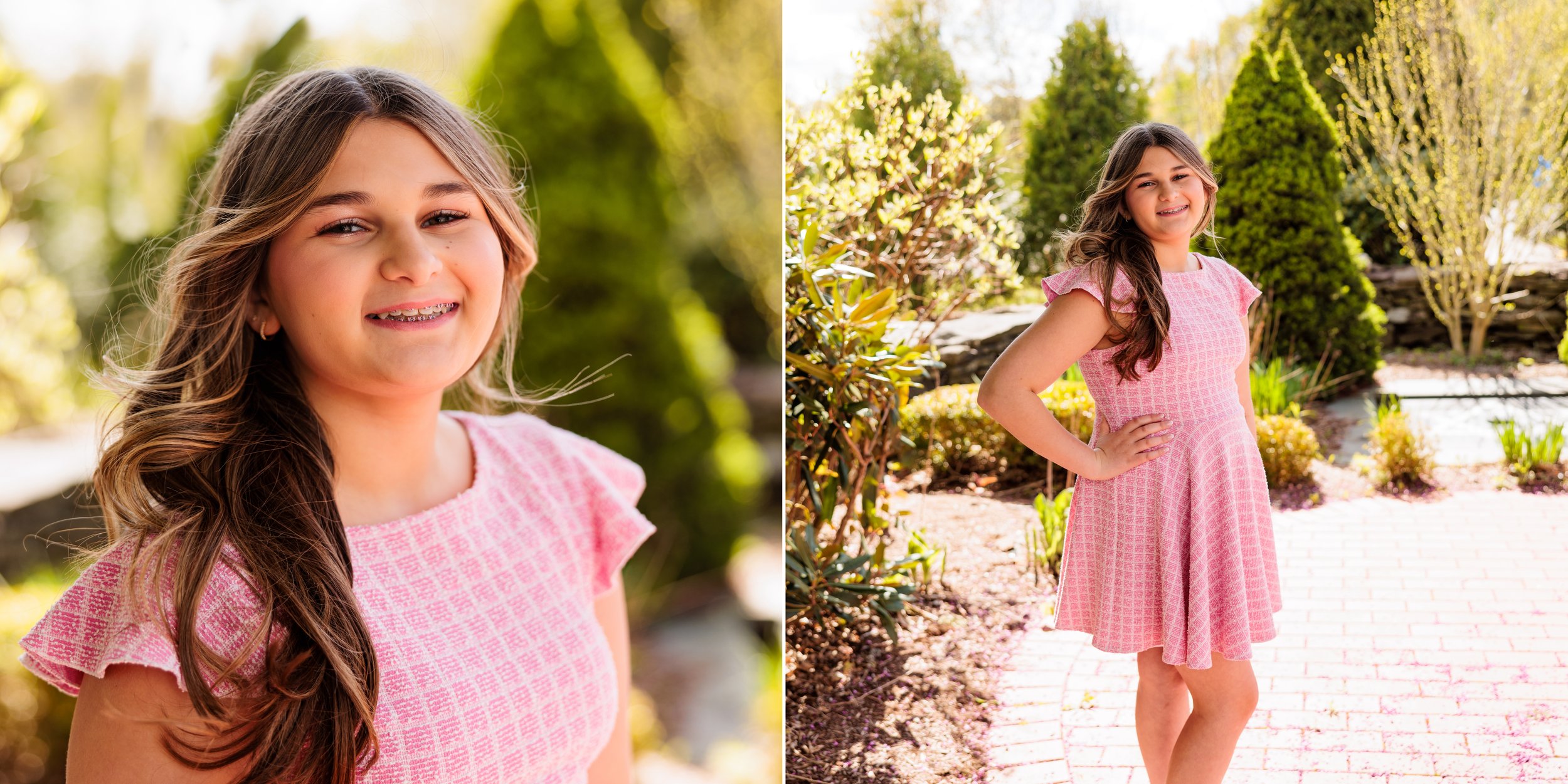 A young girl with long brown hair, wearing a pink patterned dress, smiling outdoors in a garden with sunlight and greenery.