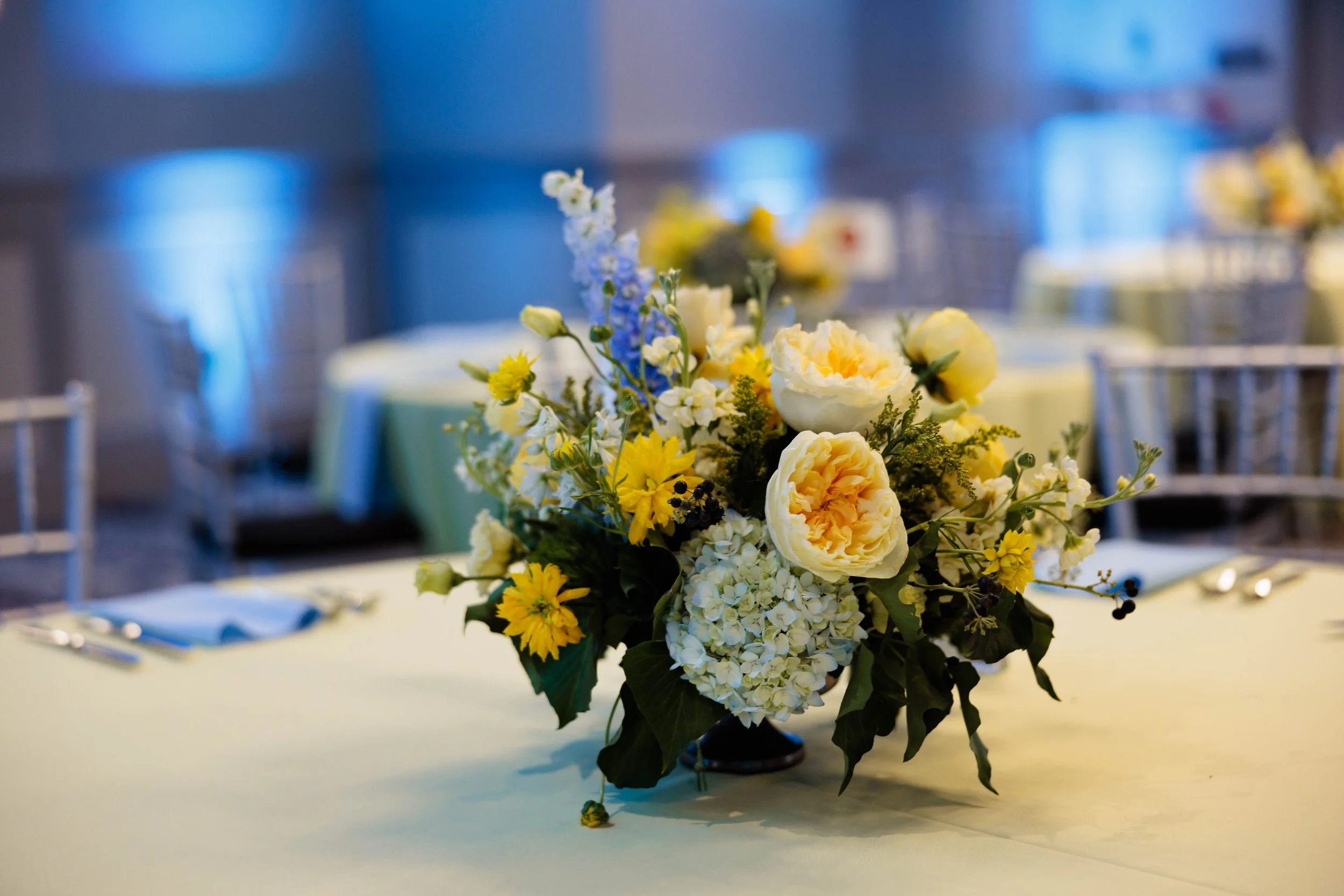 Elegant floral centerpiece with white, yellow, and purple flowers on a banquet table at an event.