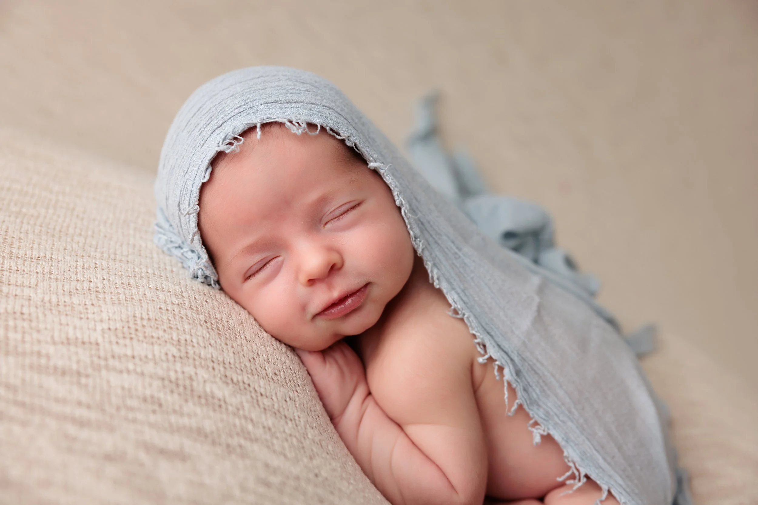 A sleeping baby with a gray hooded cloth, resting on a beige textured surface.