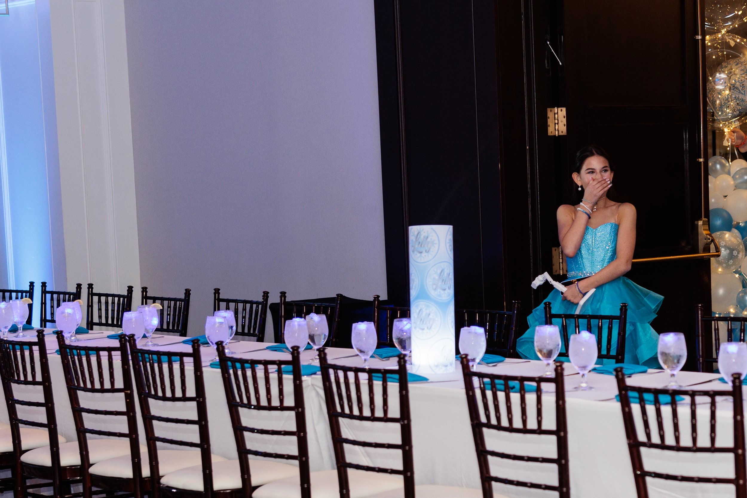 A young girl in a turquoise dress covering her mouth at a decorated event table