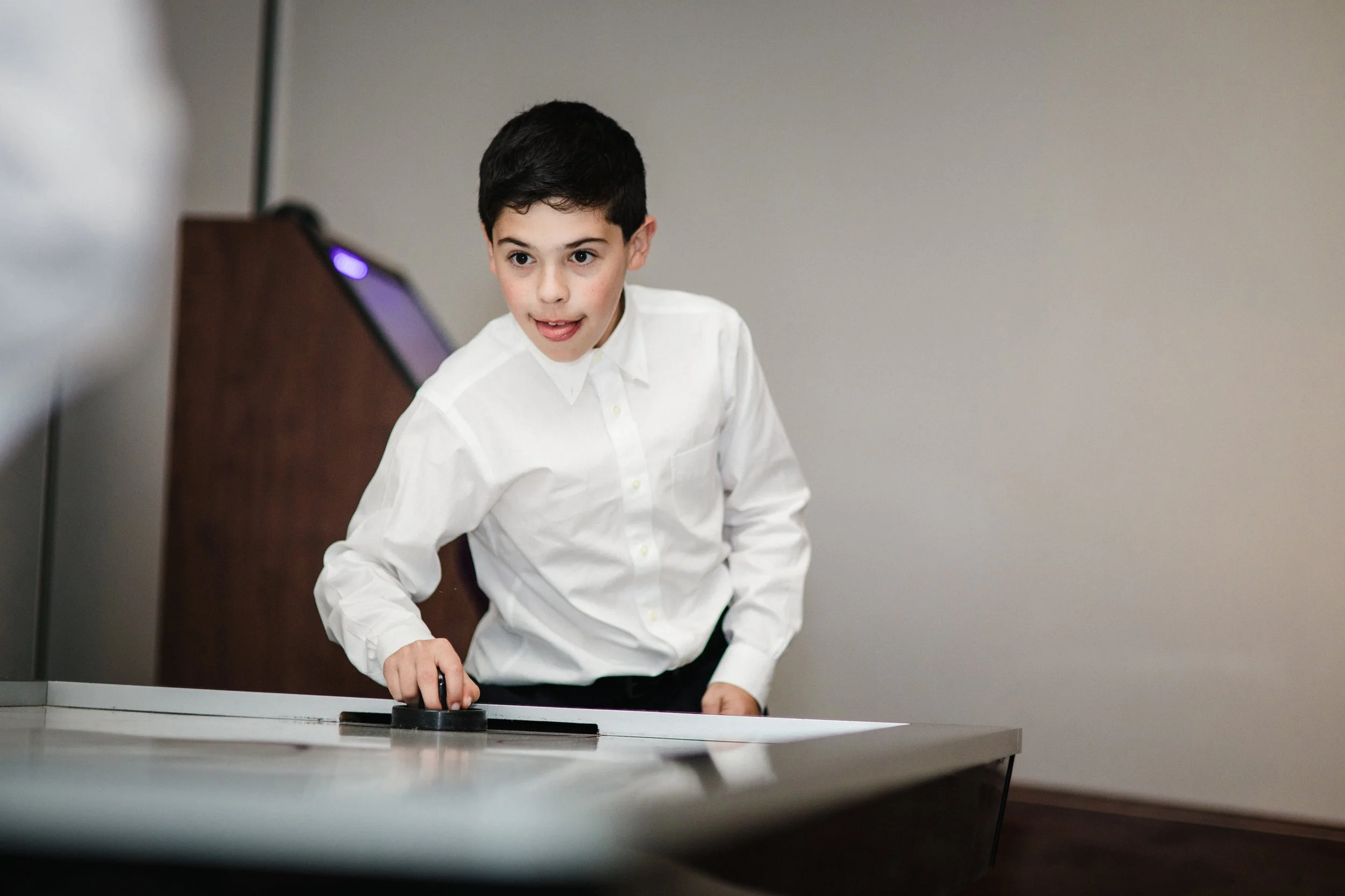 Young boy playing air hockey at a table in a room with plain beige walls.
