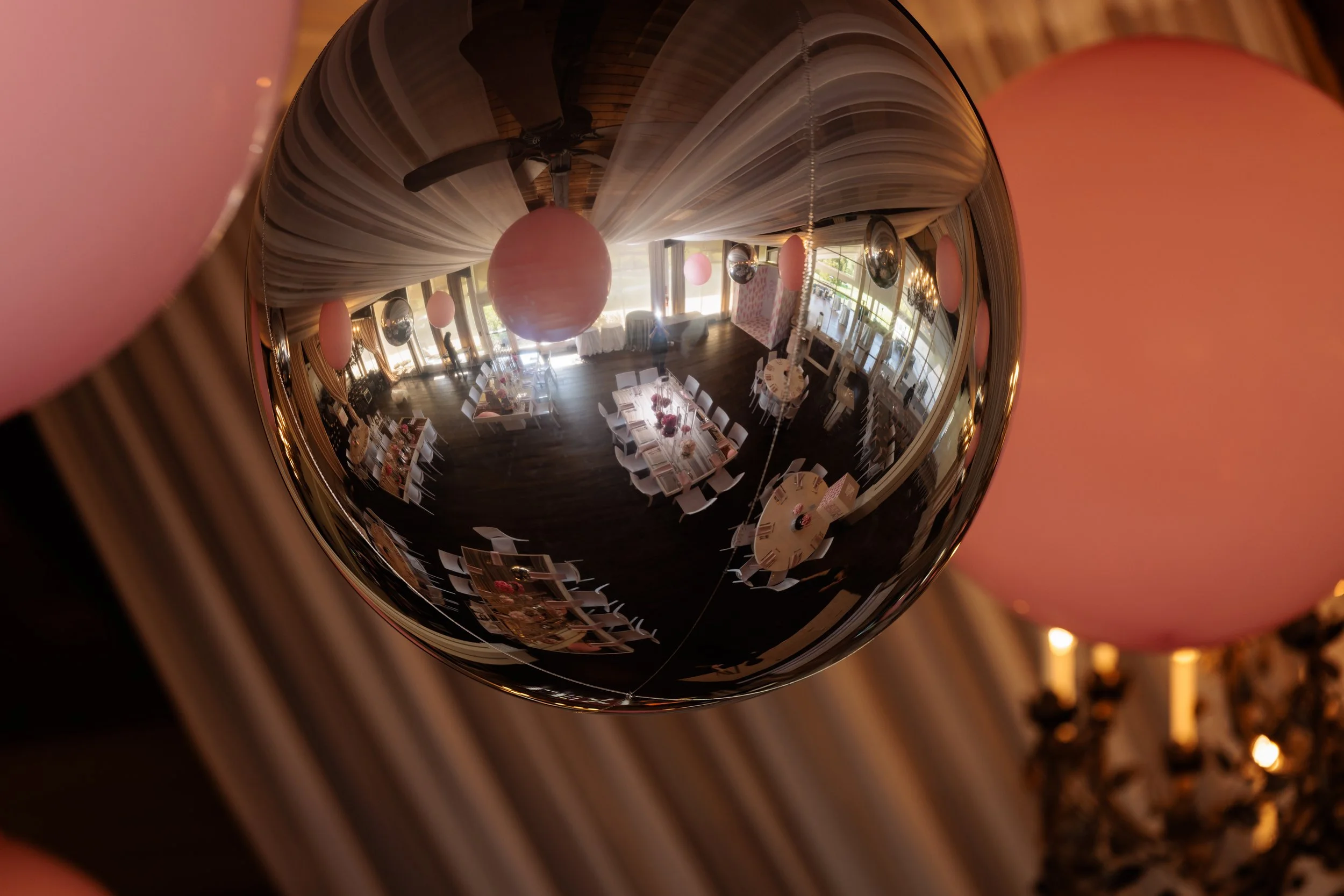 Reflection of a decorated event hall with tables set for a celebration, seen through a shiny spherical ornament hanging from the ceiling.