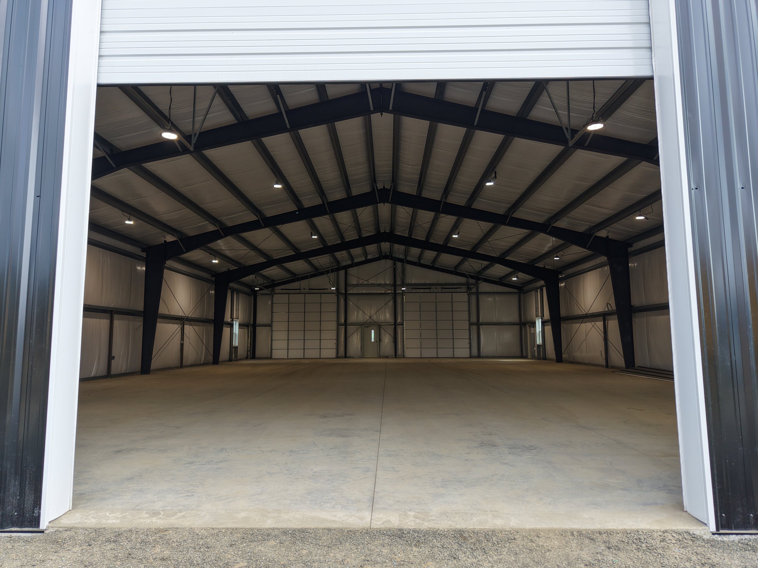 Empty commercial warehouse with open roll-up doors, high ceiling, and industrial lighting.