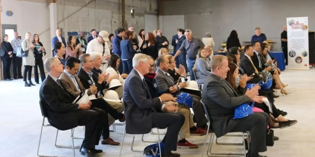 a group of professionally dressed people seating and standing in a warehouse smiling and applauding.