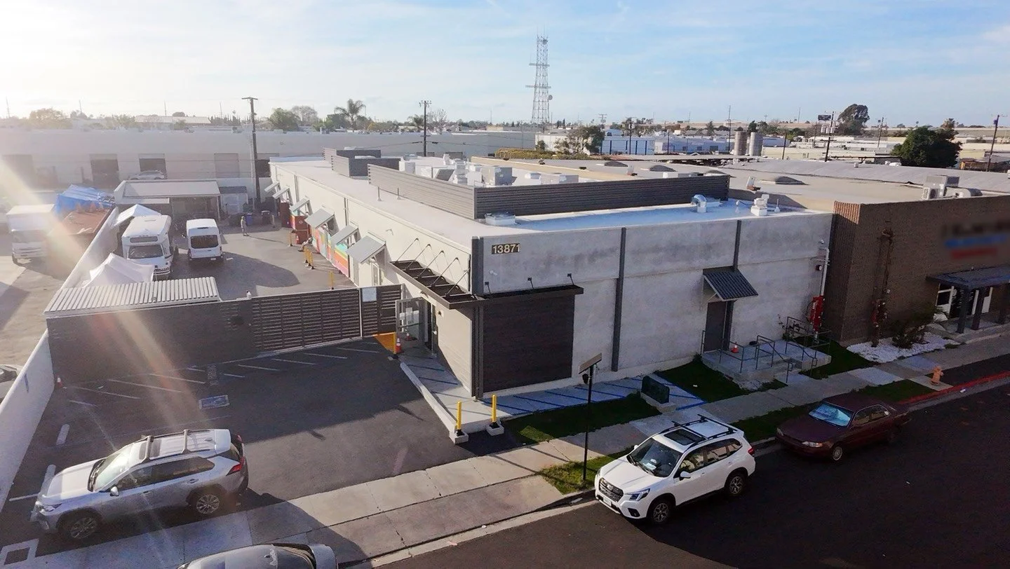 Aerial view of the Central Cities Navigation Center building at 13871, showing the modern single-story facility, front entrance with the colorful mural visible, service vans in the parking area, and surrounding Garden Grove neighborhood.
