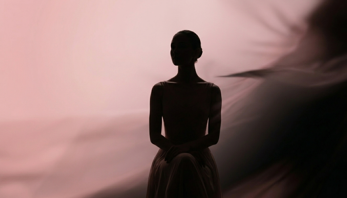 Silhouette of a woman sitting with her hands on her lap, against a pink and black blurred background.