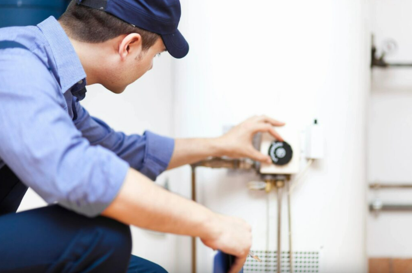 A technician adjusting a thermostat on an indoor wall.