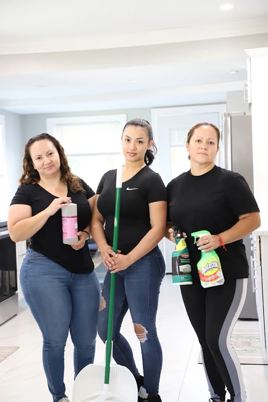 Carmen's House Cleaning LLC's staff members standing in a bright kitchen, holding cleaning supplies, with a mop in the center.