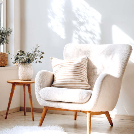 Cozy armchair with striped pillow beside a small wooden table and potted plant in a sunlit therapy office.