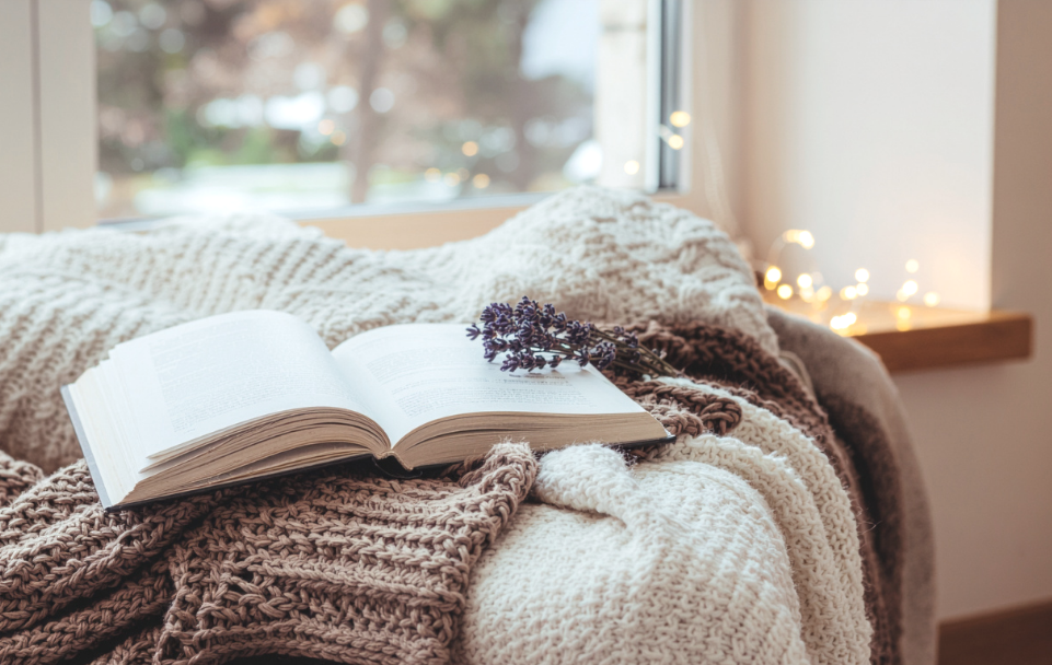 Open book on a cozy knit blanket by a window with a sprig of lavender, representing reflection and a calm, supportive therapy environment.