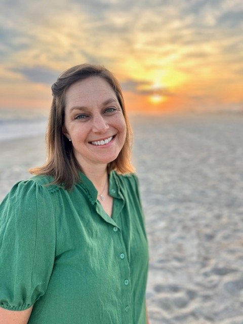 Smiling woman in green shirt at the beach during sunset.