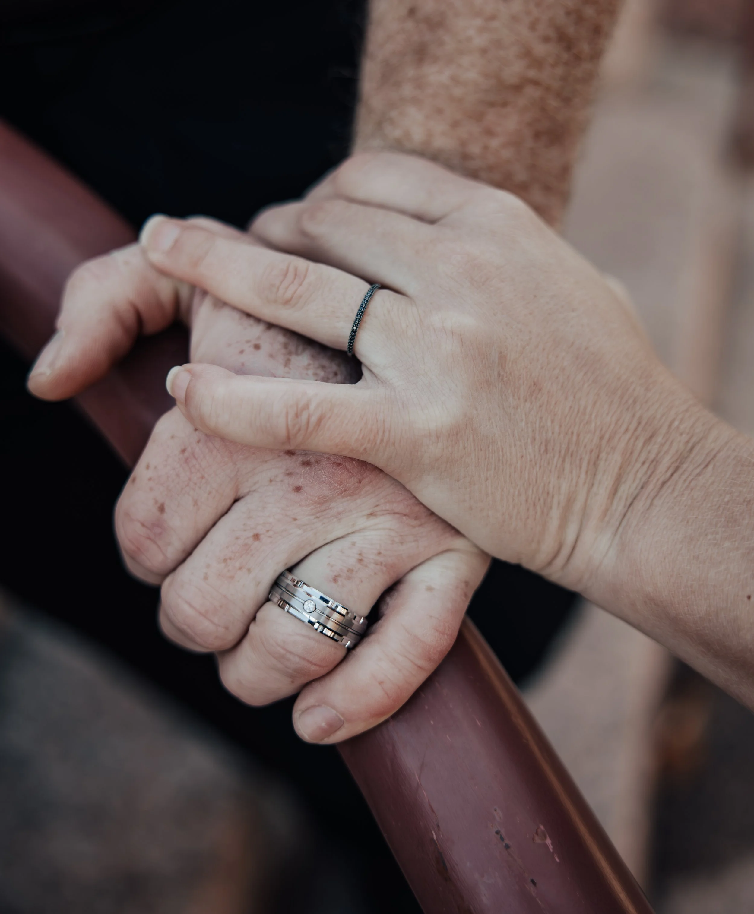 Close-up of two people holding hands, with one person wearing a diamond engagement ring, smiling in the background.