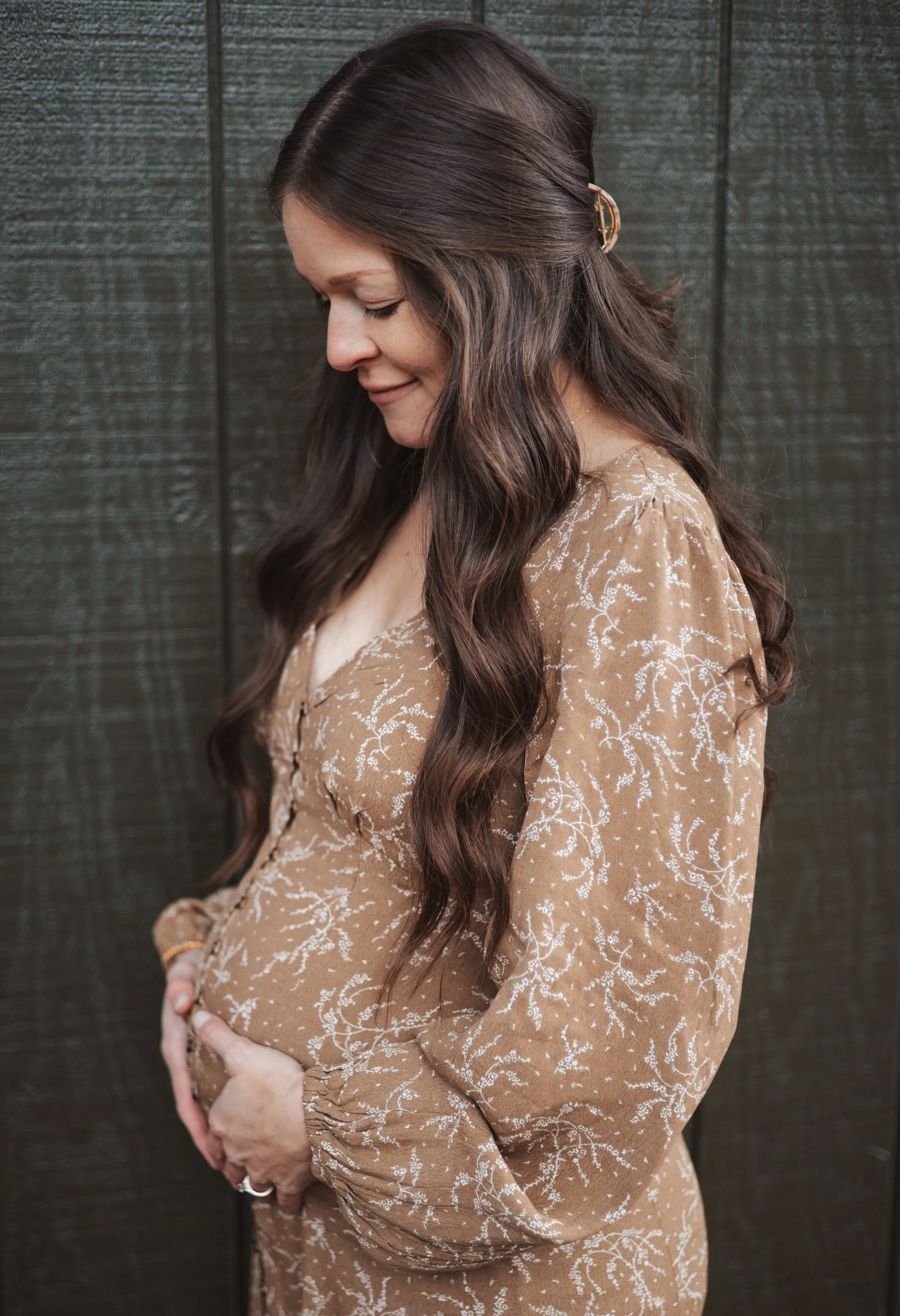 A pregnant woman standing on a beach at sunset, smiling and holding her belly.