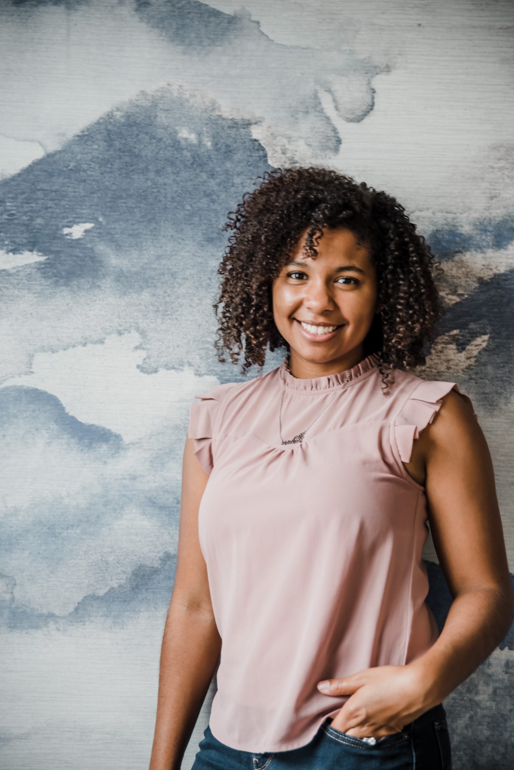 A woman with curly hair smiling and standing in front of a large speaker with a black and gray abstract design.