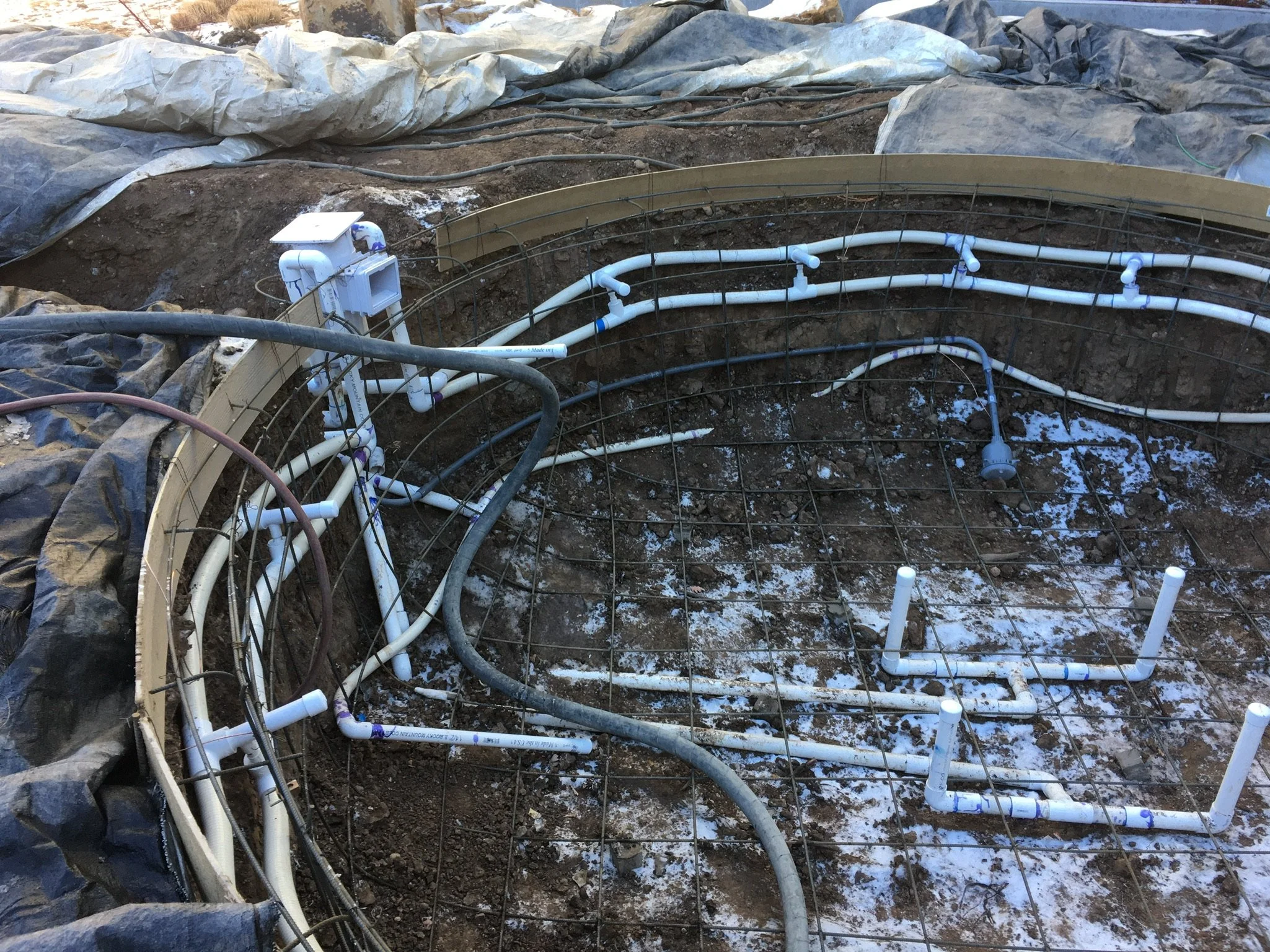Construction site with piping, wiring, and reinforcement grid for concrete foundation.