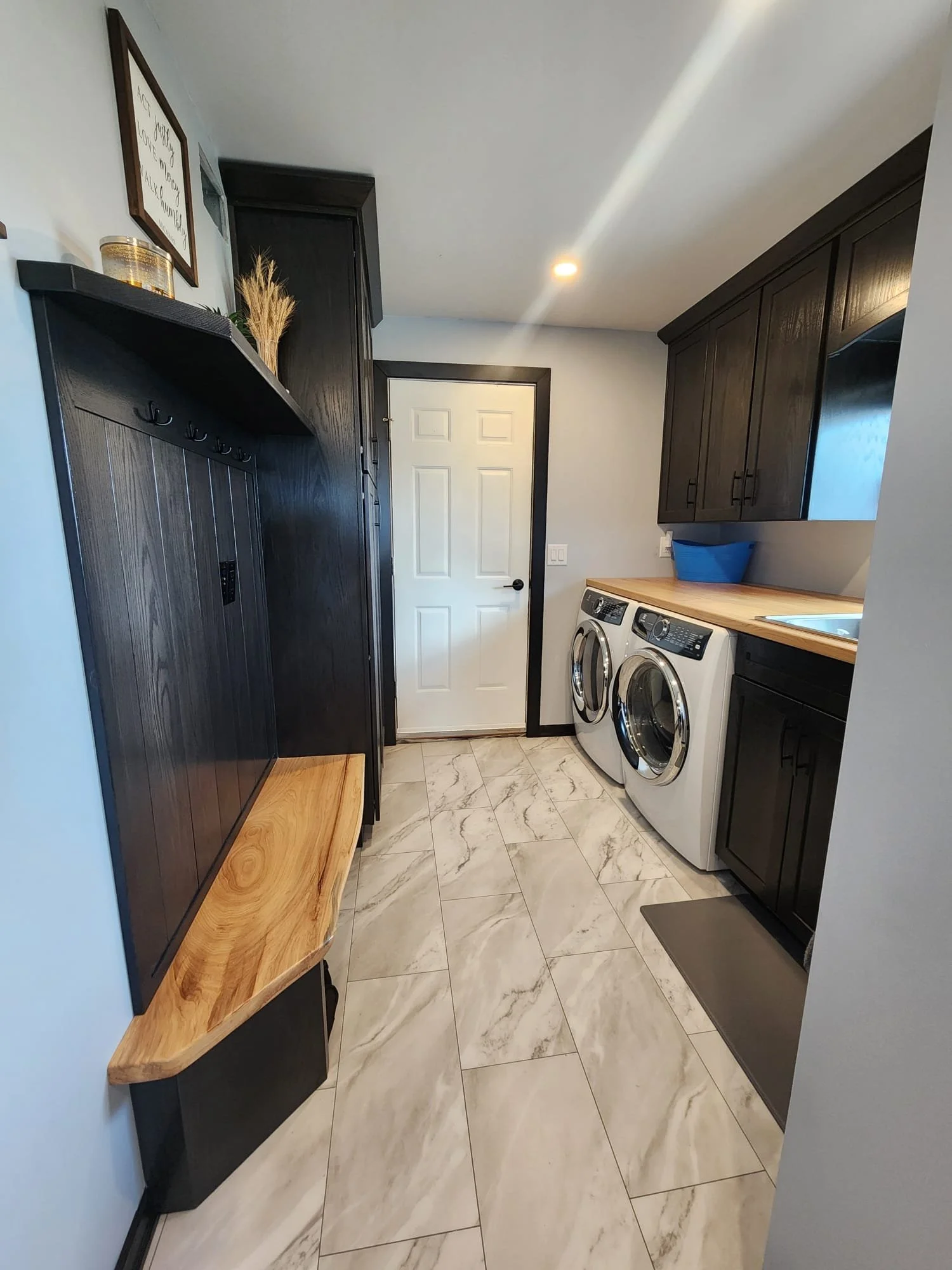 Laundromat room with dark wooden cabinets, a white front-loading washer and dryer, a wooden countertop, and a laundry basket.