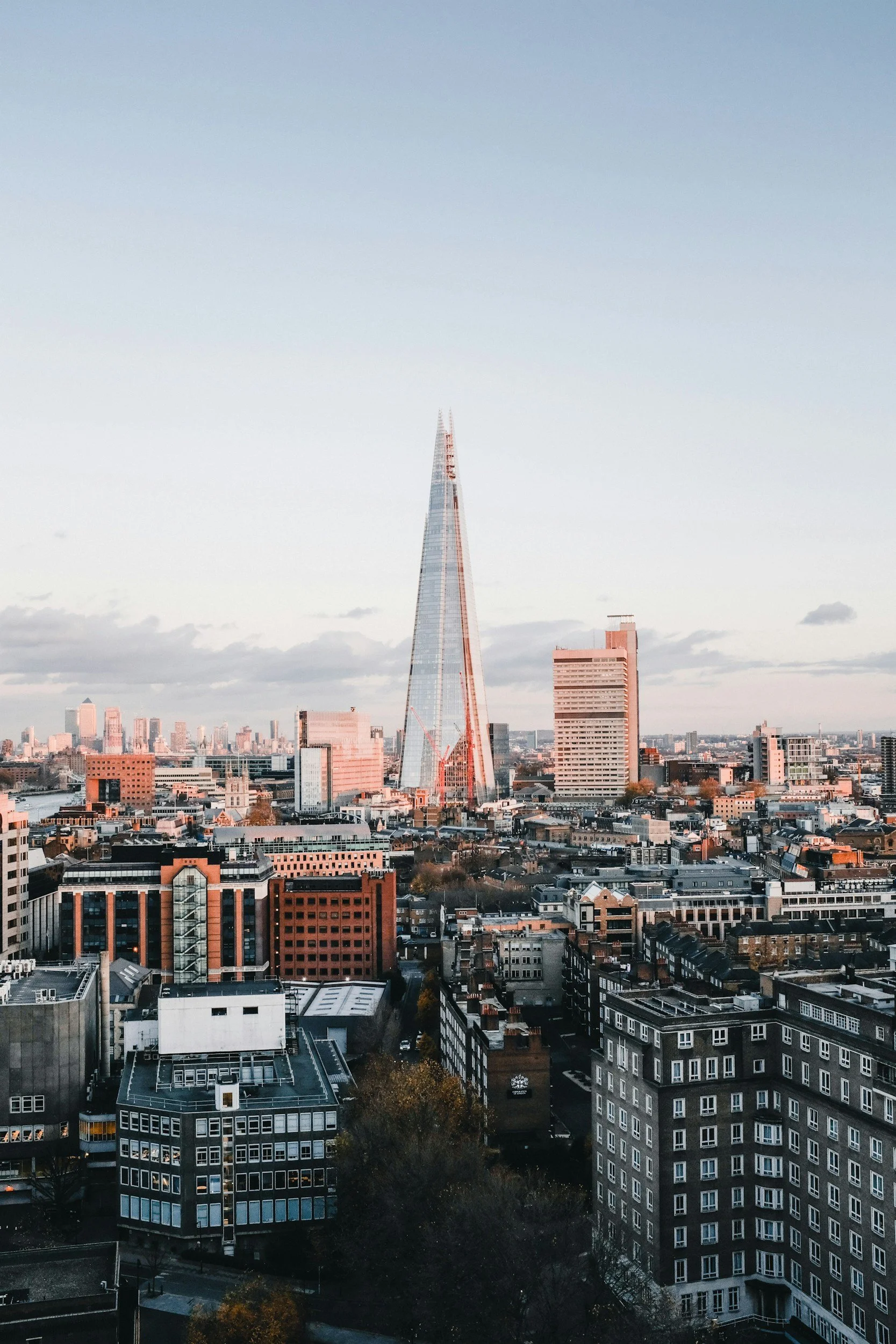 A city skyline featuring the Shard skyscraper and other high-rise buildings under a partly cloudy sky during dusk.