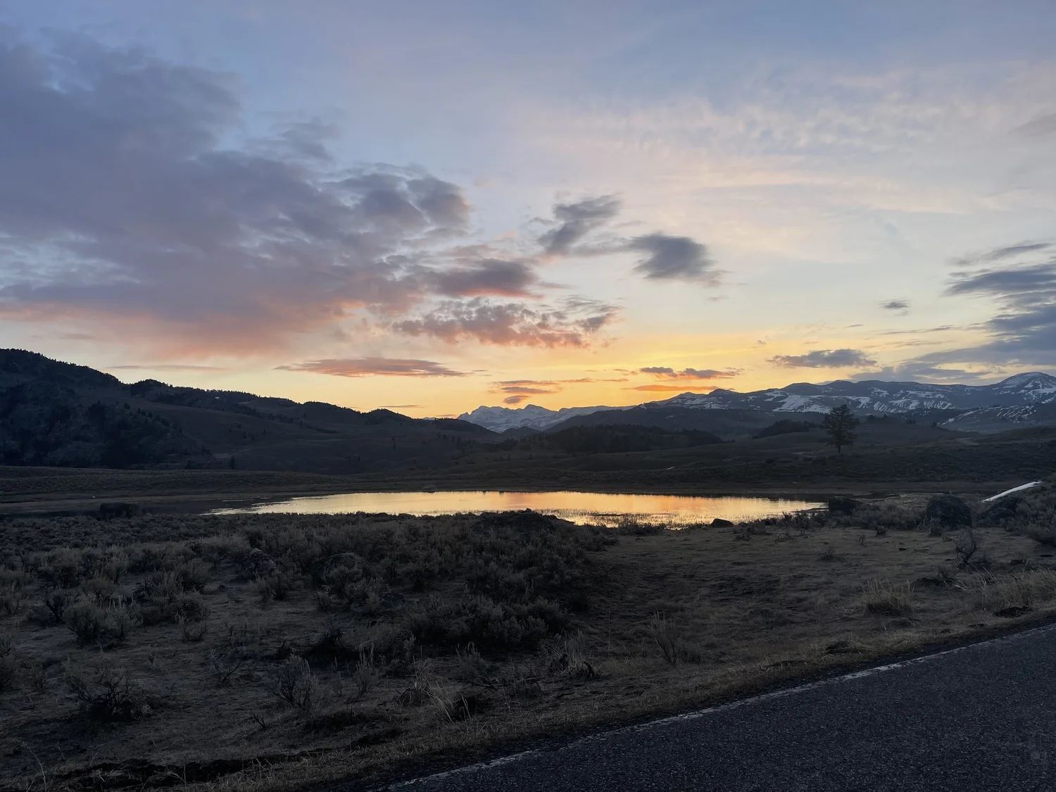 Sunset over Lamar Valley Yellowstone with pond reflecting orange sky and snow-capped peaks
