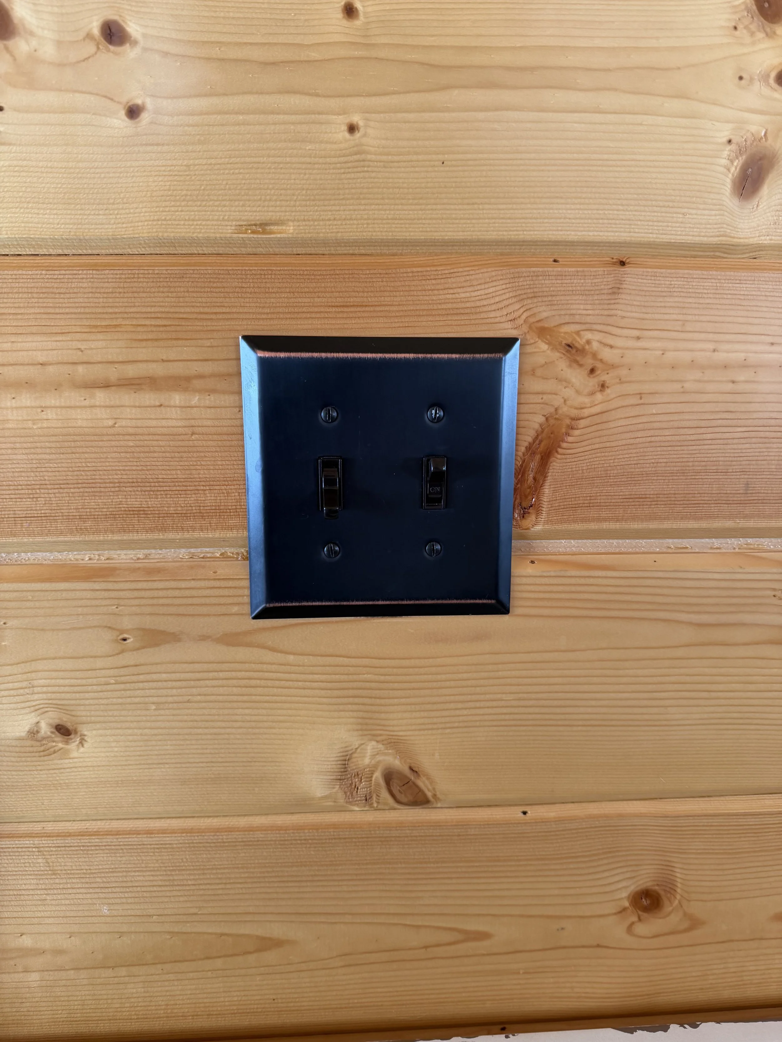 A black double light switch installed on a wood-paneled wall.