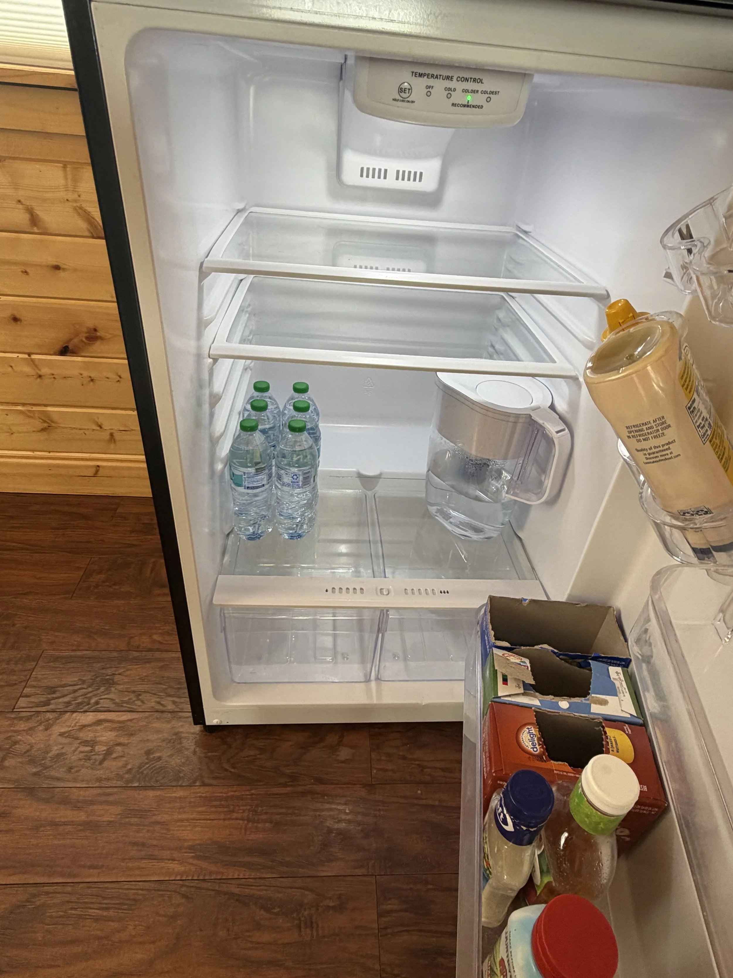 Open empty refrigerator with a few water bottles and a water pitcher on the shelves, and condiments and food jars in the door.