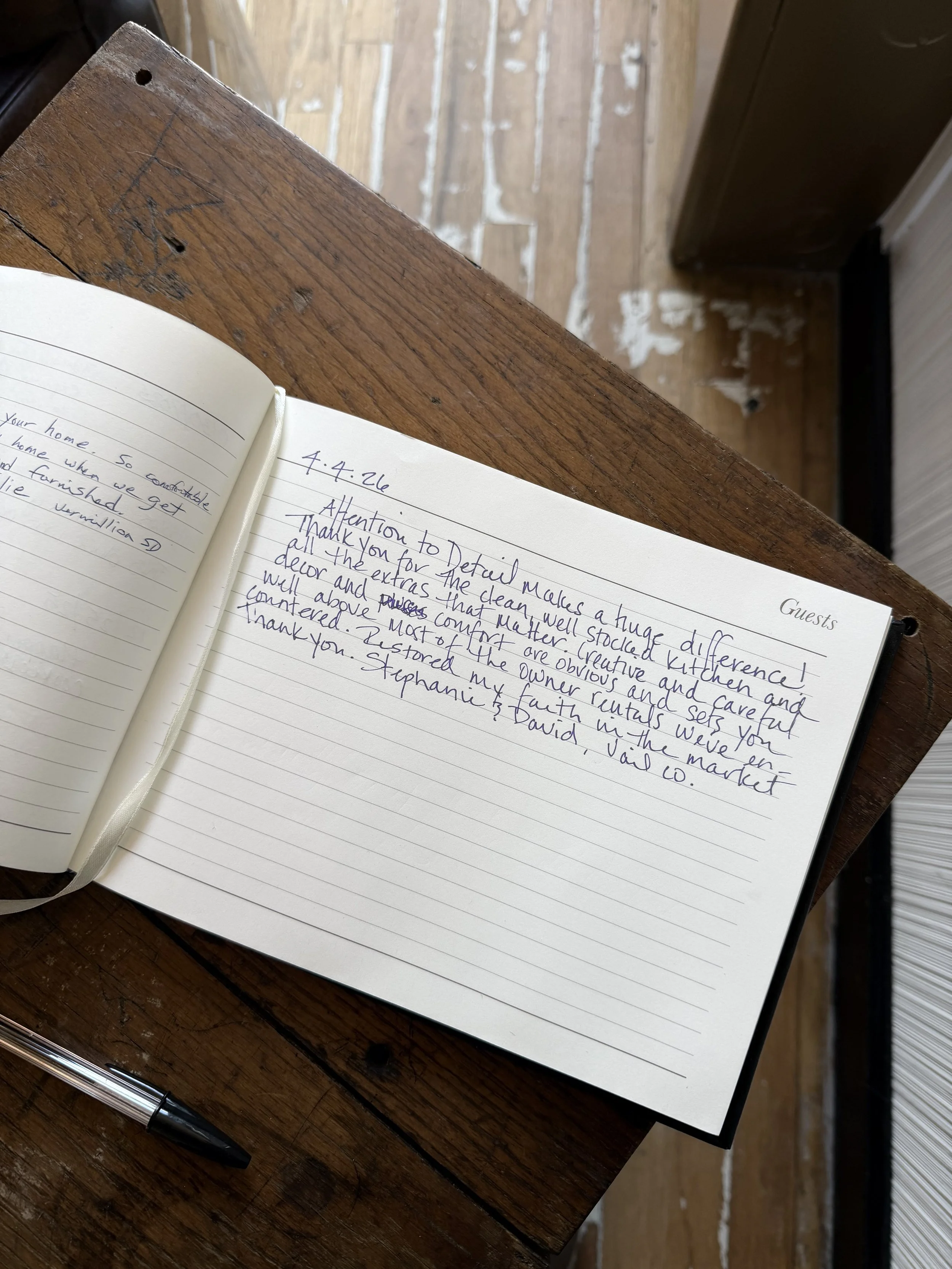 Open guestbook with handwritten notes and a pen on a weathered wooden table.