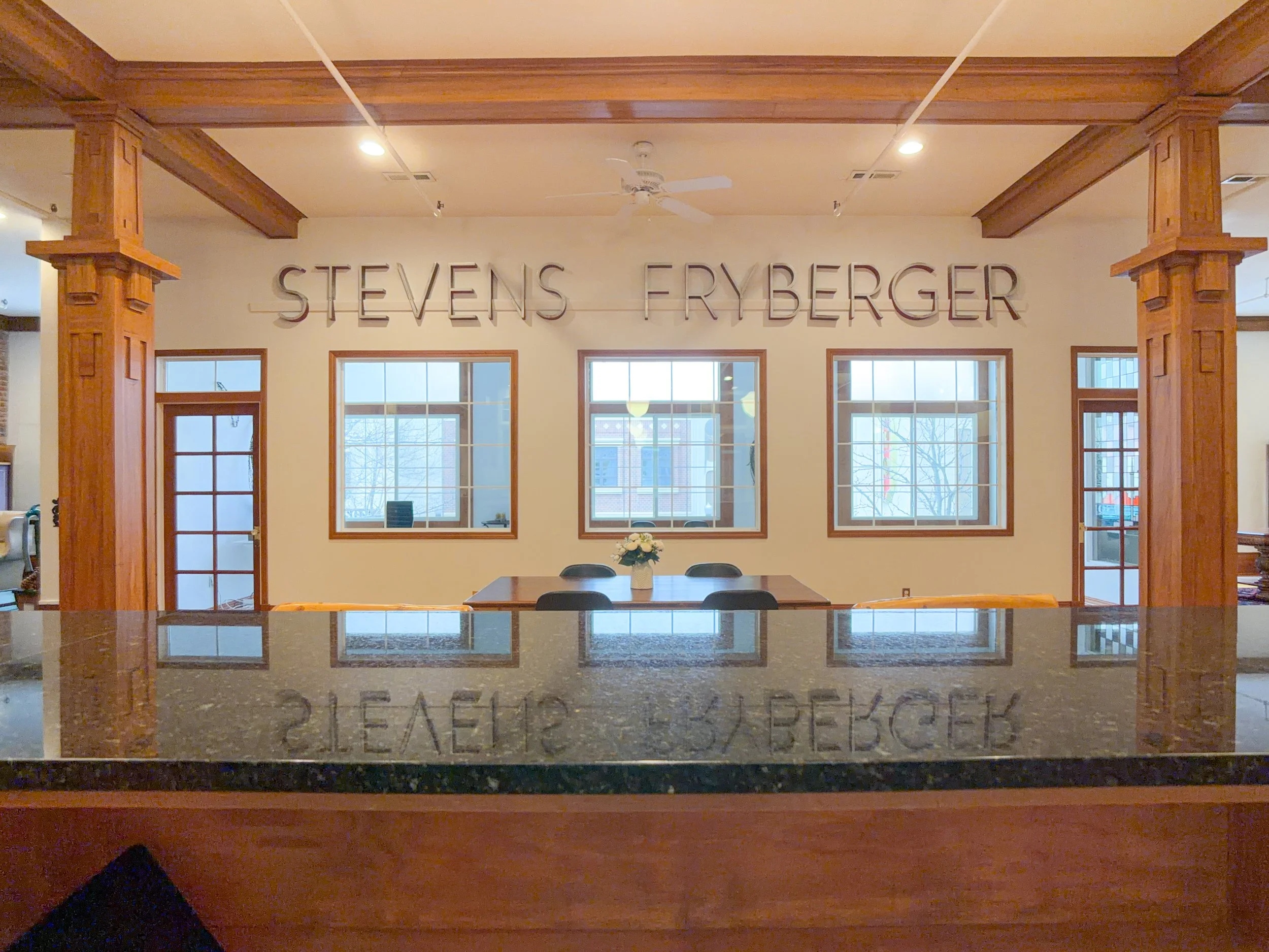 I Interior with exposed wood beams and "Stevens Fryberger" lettering, set with a table, chairs, and flowers.