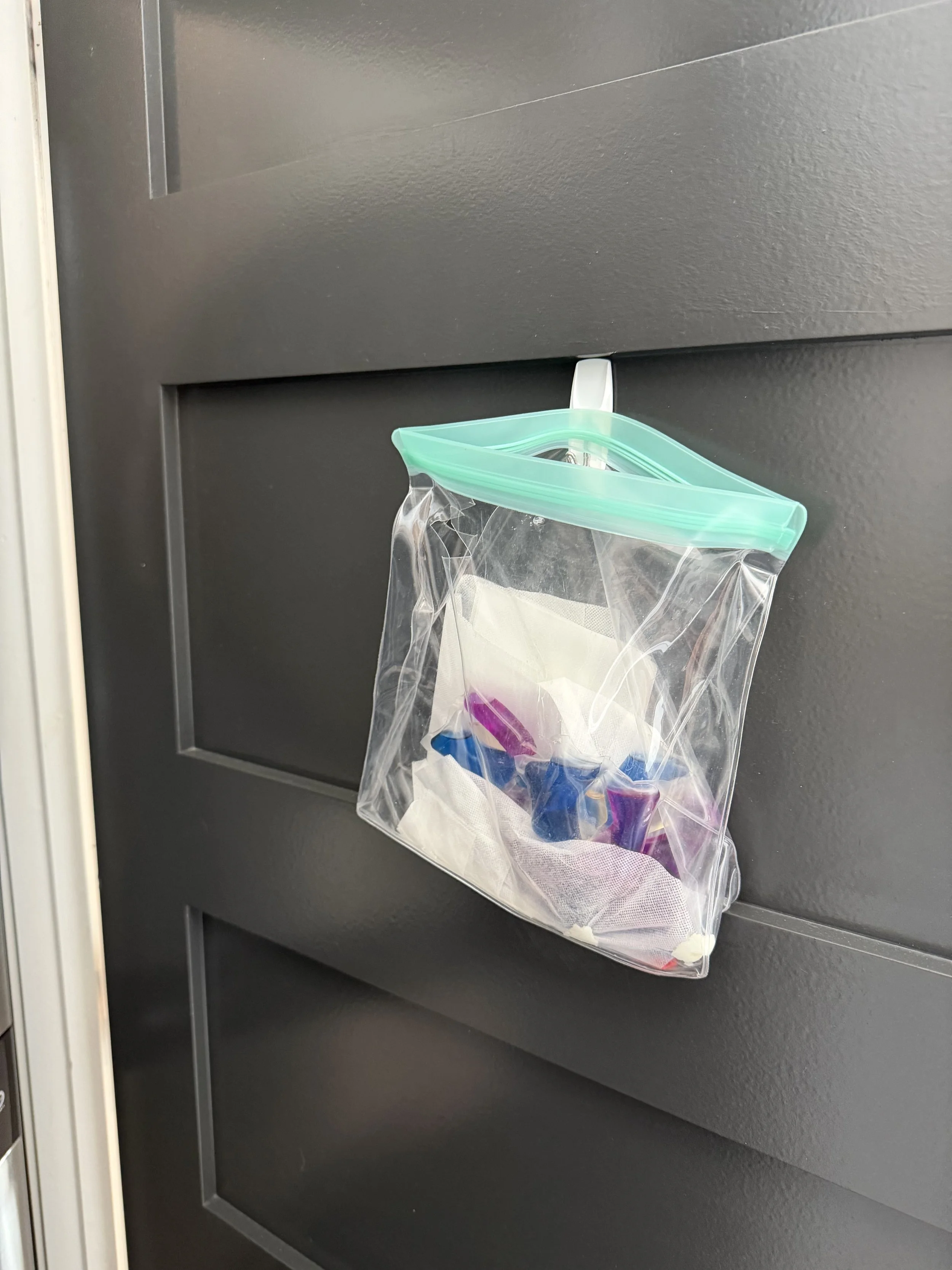 A plastic zippered bag hanging on a door handle with medication blister packs inside.
