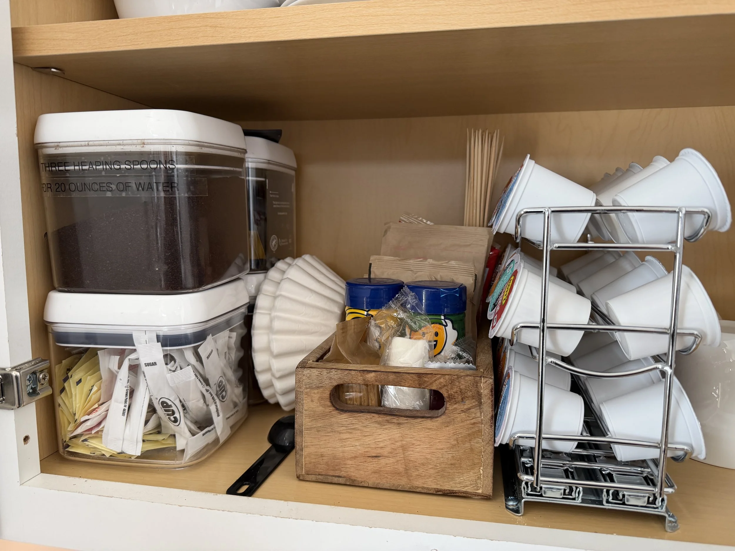 Kitchen cabinet with sugar, water, coffee cups, and utensils.