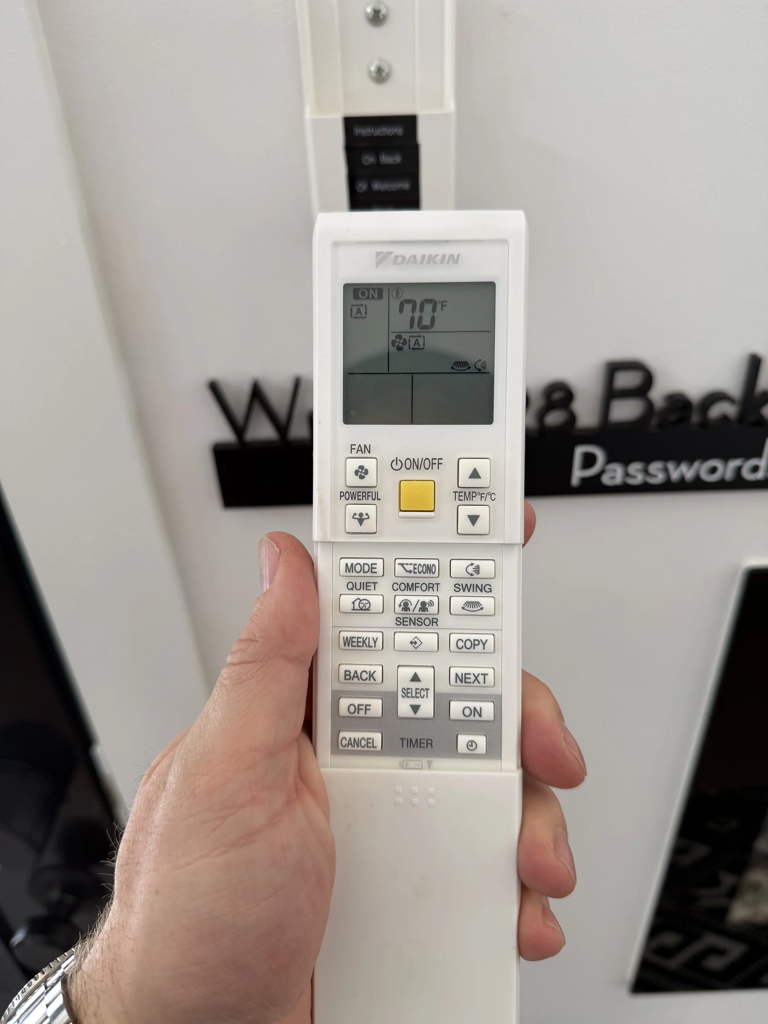 A hand holding a white remote control for an air conditioning unit, with a digital display showing 70°F temperature.