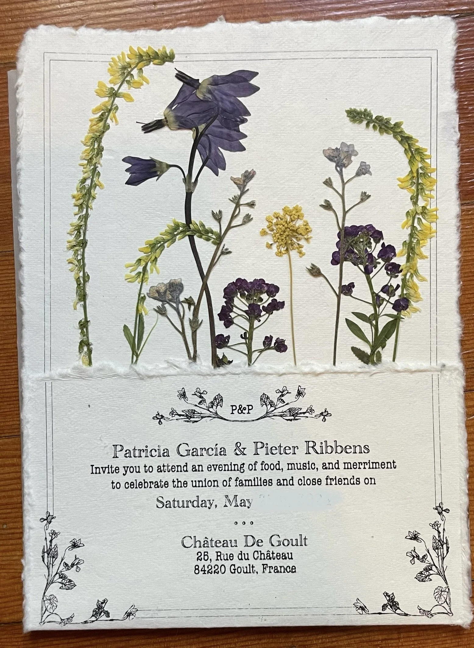 Invitation card with pressed flowers and text about an event celebrating family and friends, hosted by Patricia Garcia and Pieter Ribbens at Château De Gault, France.