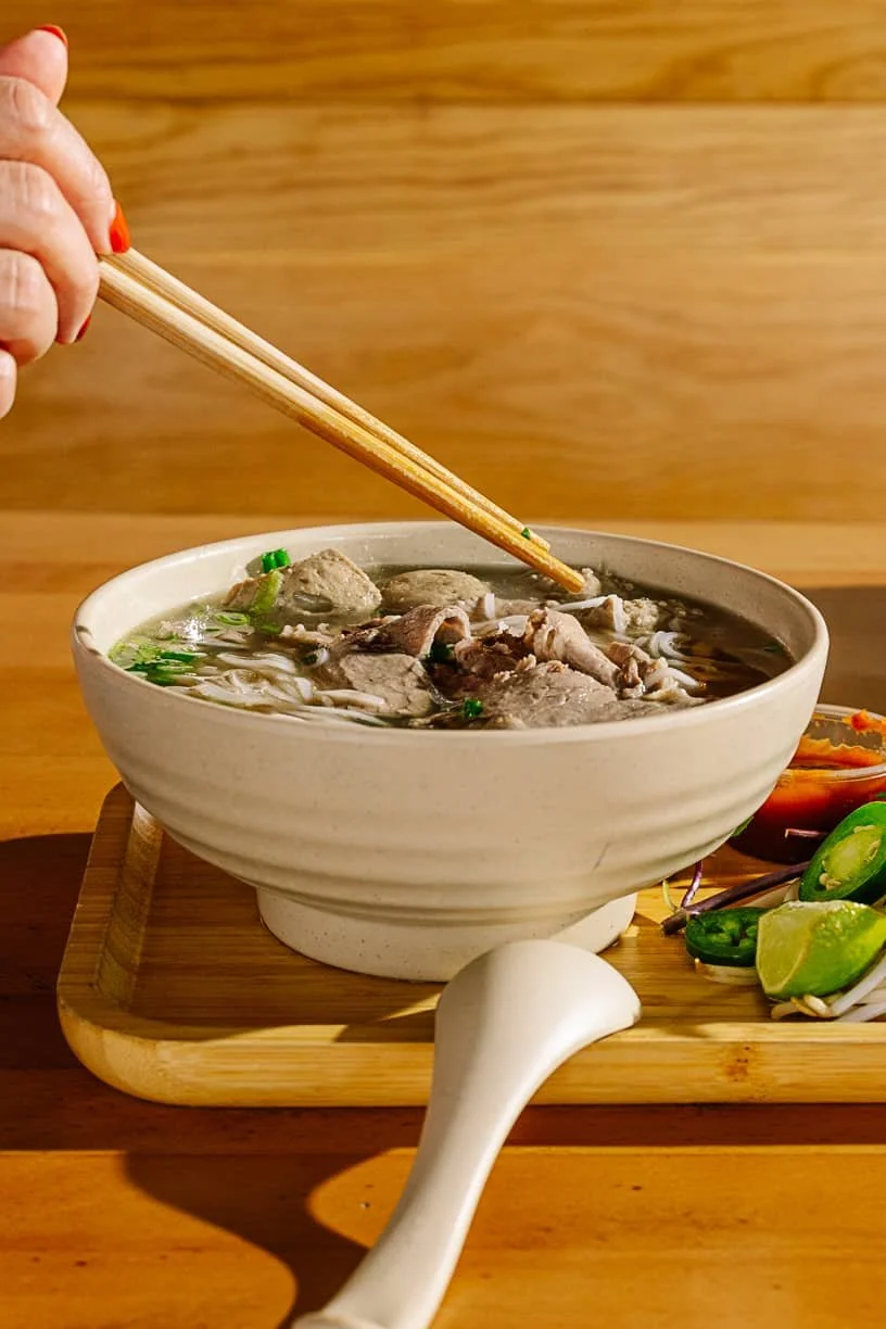 Person using chopsticks by bowl of pho from Ngon