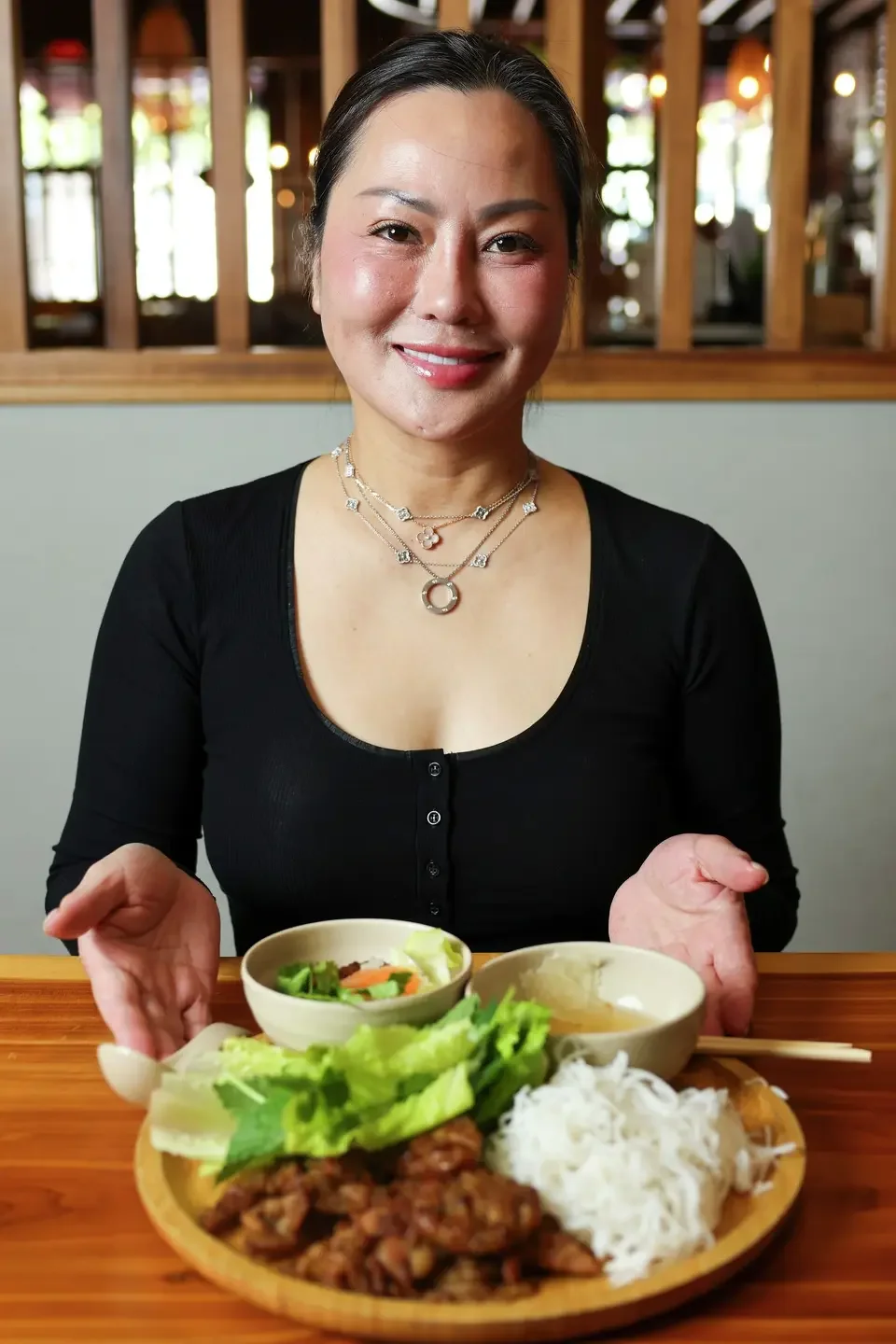 Carol Nguyen smiling while pushing a plate of Bun Cha Hanoi towards the camera