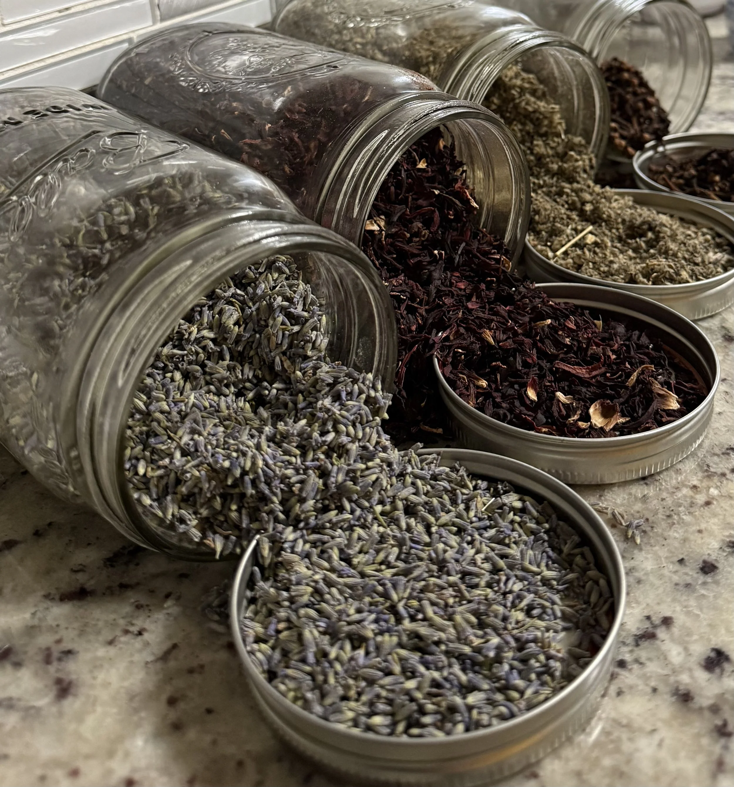 Several glass jars and small bowls filled with dried herbs and spices, arranged on a countertop.