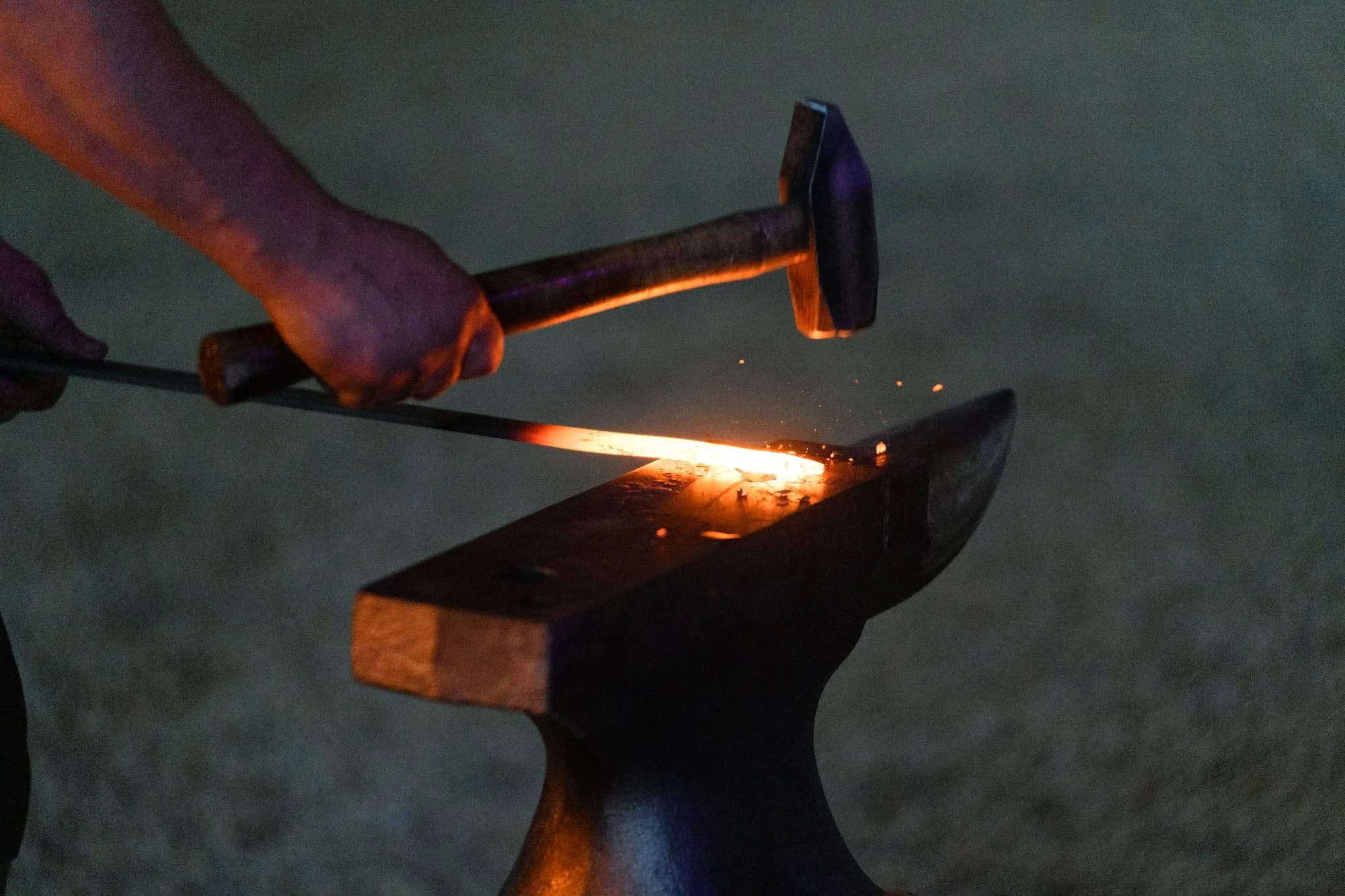 Hammer striking glowing hot metal on an anvil during a blacksmithing demonstration
