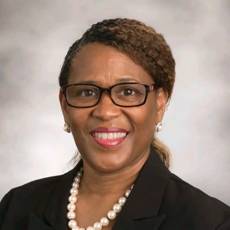 A badge with a helmet, shield, and various symbols, surrounded by leaves, featuring Greek text at the bottom.