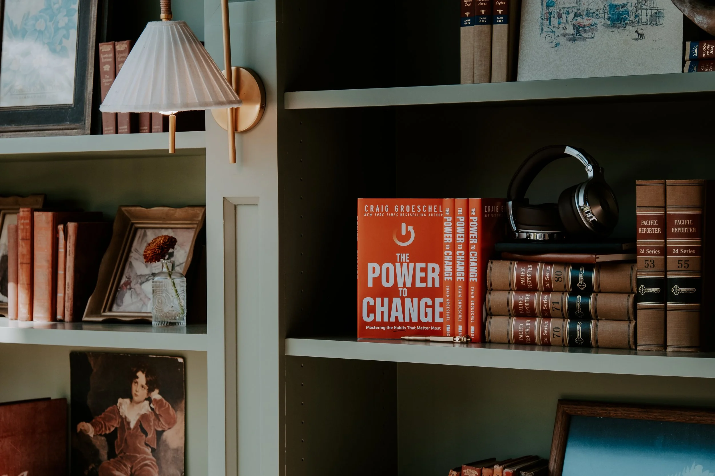 Bookshelf with a pair of black headphones, a red book titled "The Power to Change" by Craig Groeschel, and various other books and decorative items.